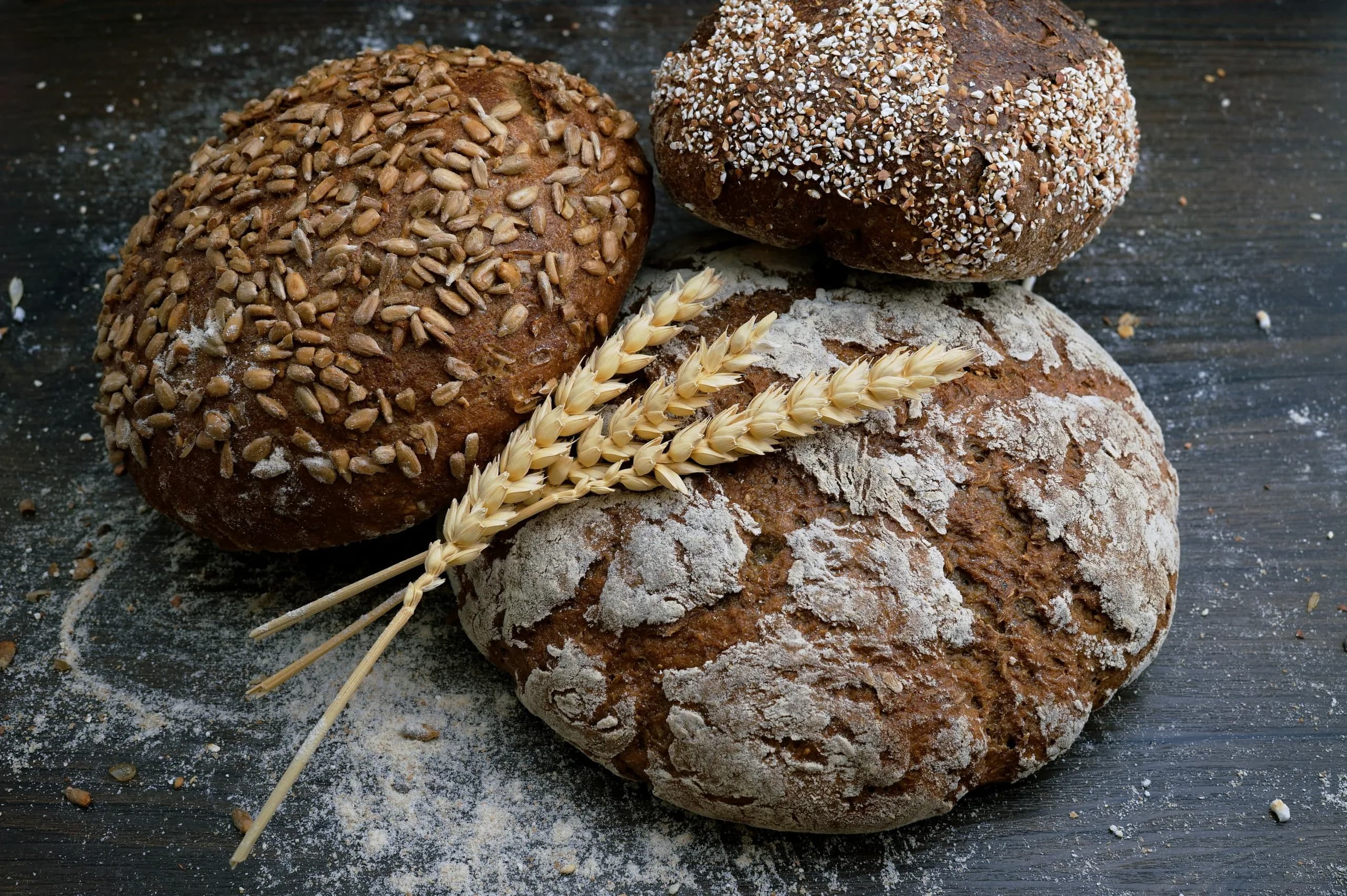 Three dark rustic loaves dusted with flour beside ears of wheat