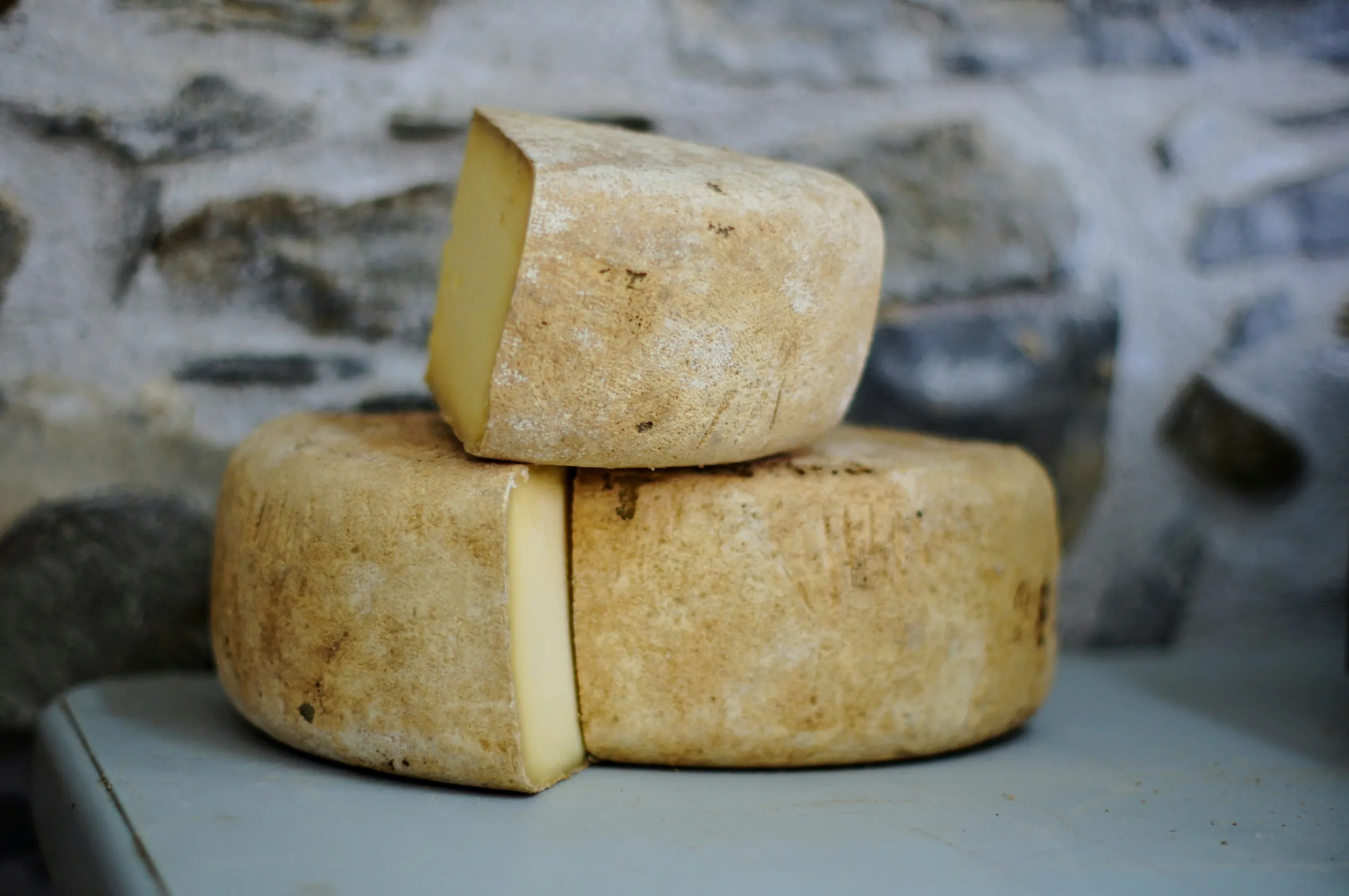 Two cut wheels of mountain cheese resting against a stone wall