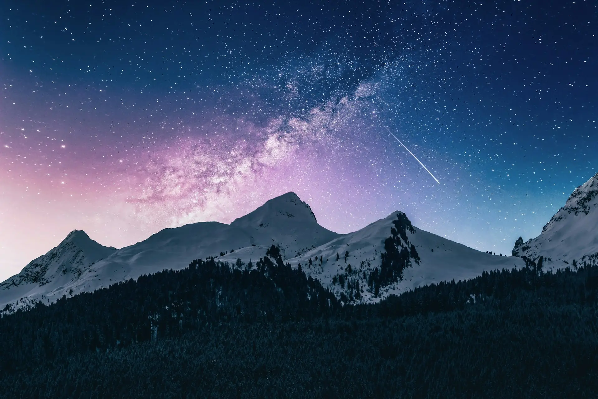 Snow-covered peaks under a starry night sky with the Milky Way