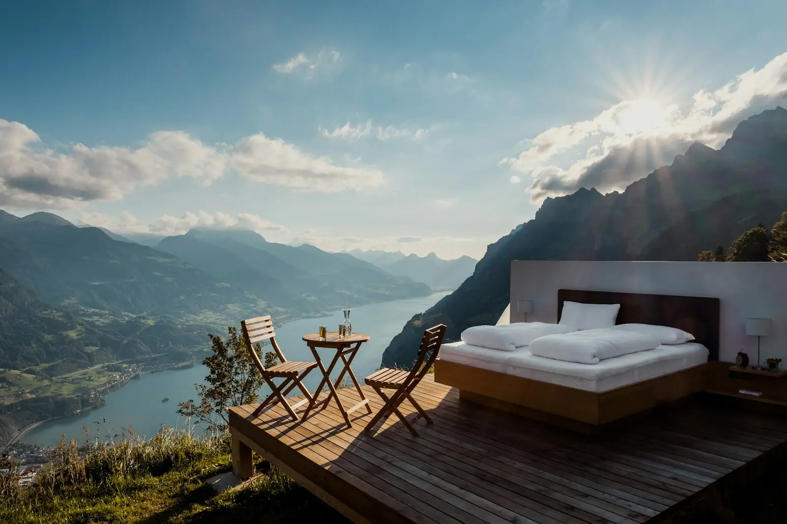 A double bed on an open timber deck high above an alpine lake