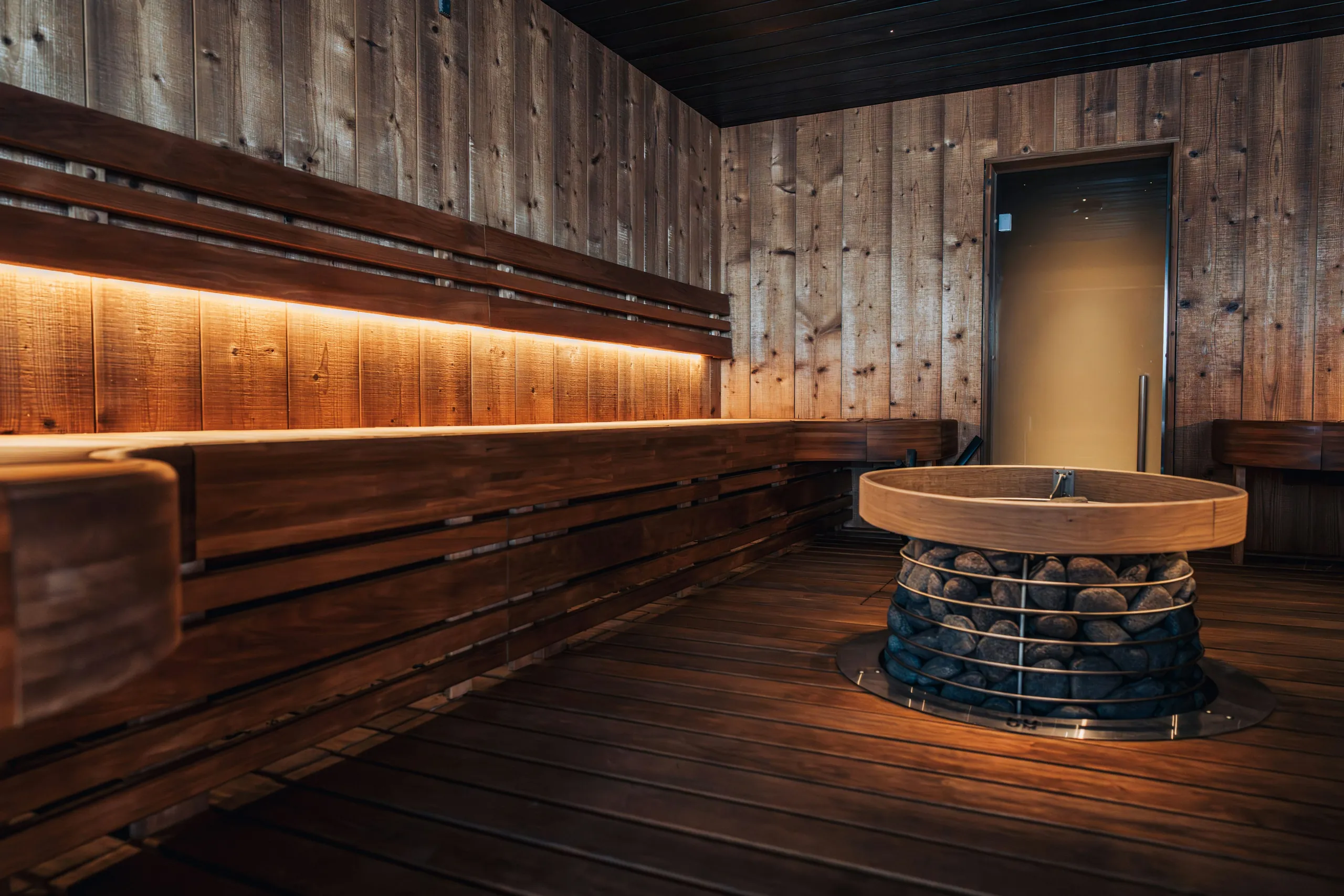 A dark cedar sauna with a round stone heater