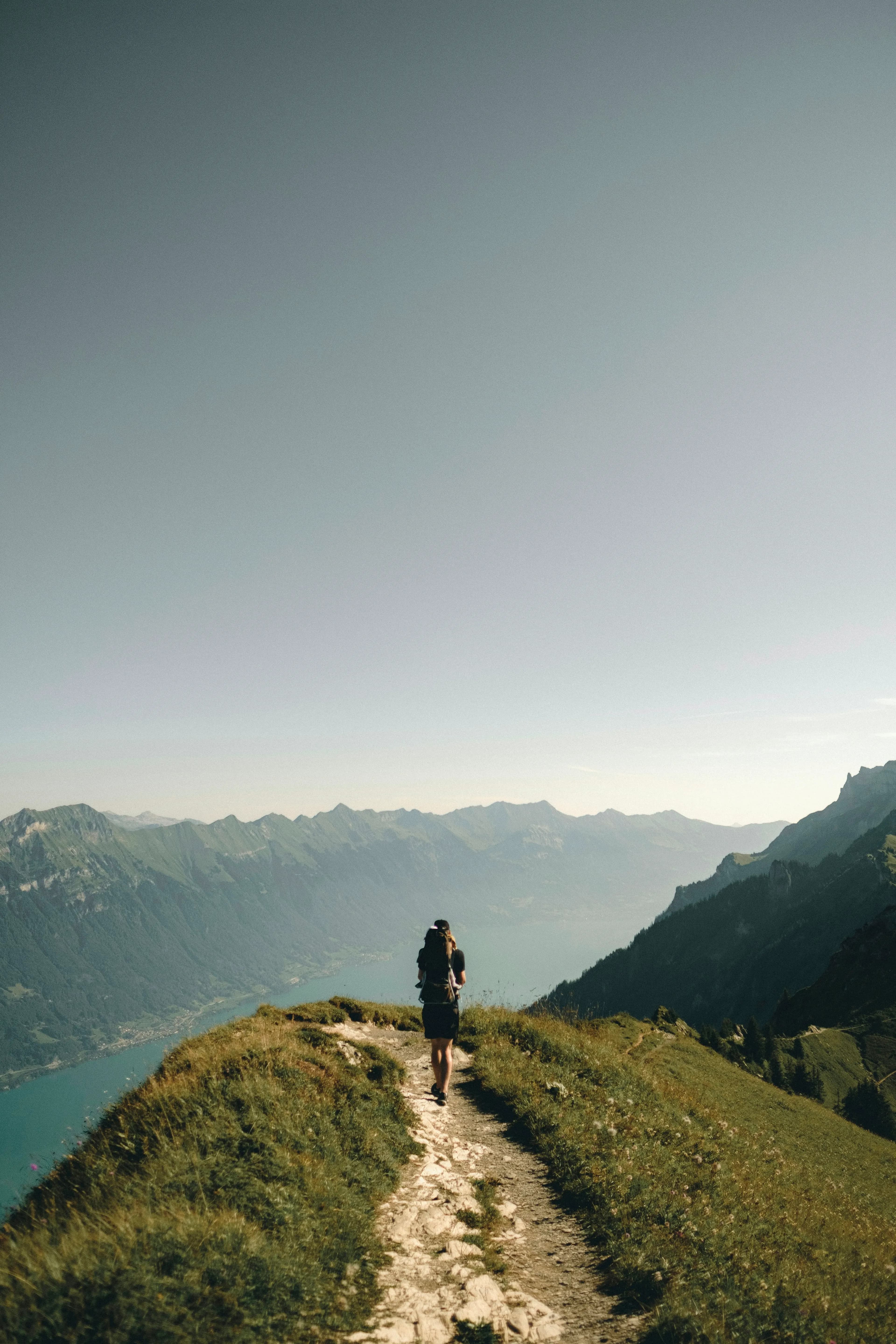 A lone walker on a narrow ridge path high above a long green valley