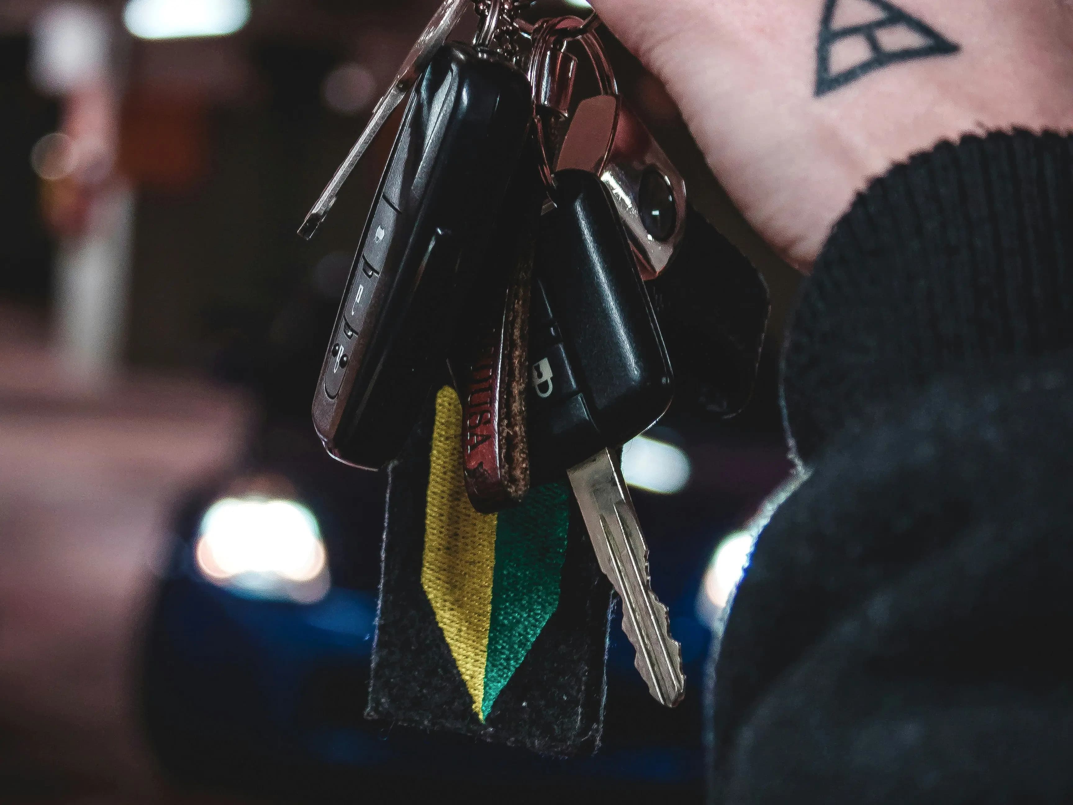 A bunch of car keys held in a hand at night, headlights burning out of focus behind them