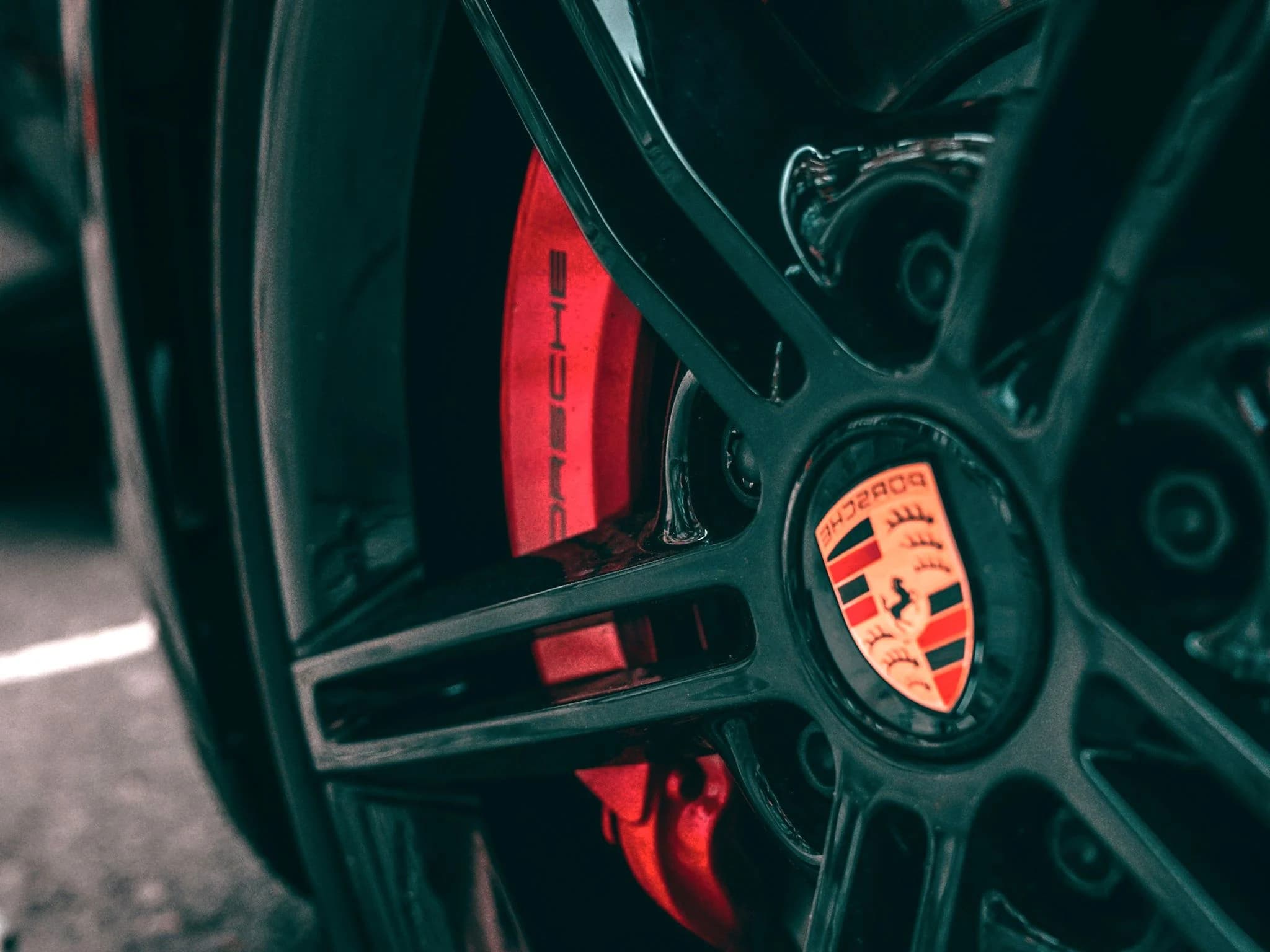 Close view of a Porsche wheel, the crest on the centre cap and a red brake caliper reading Porsche behind the spokes