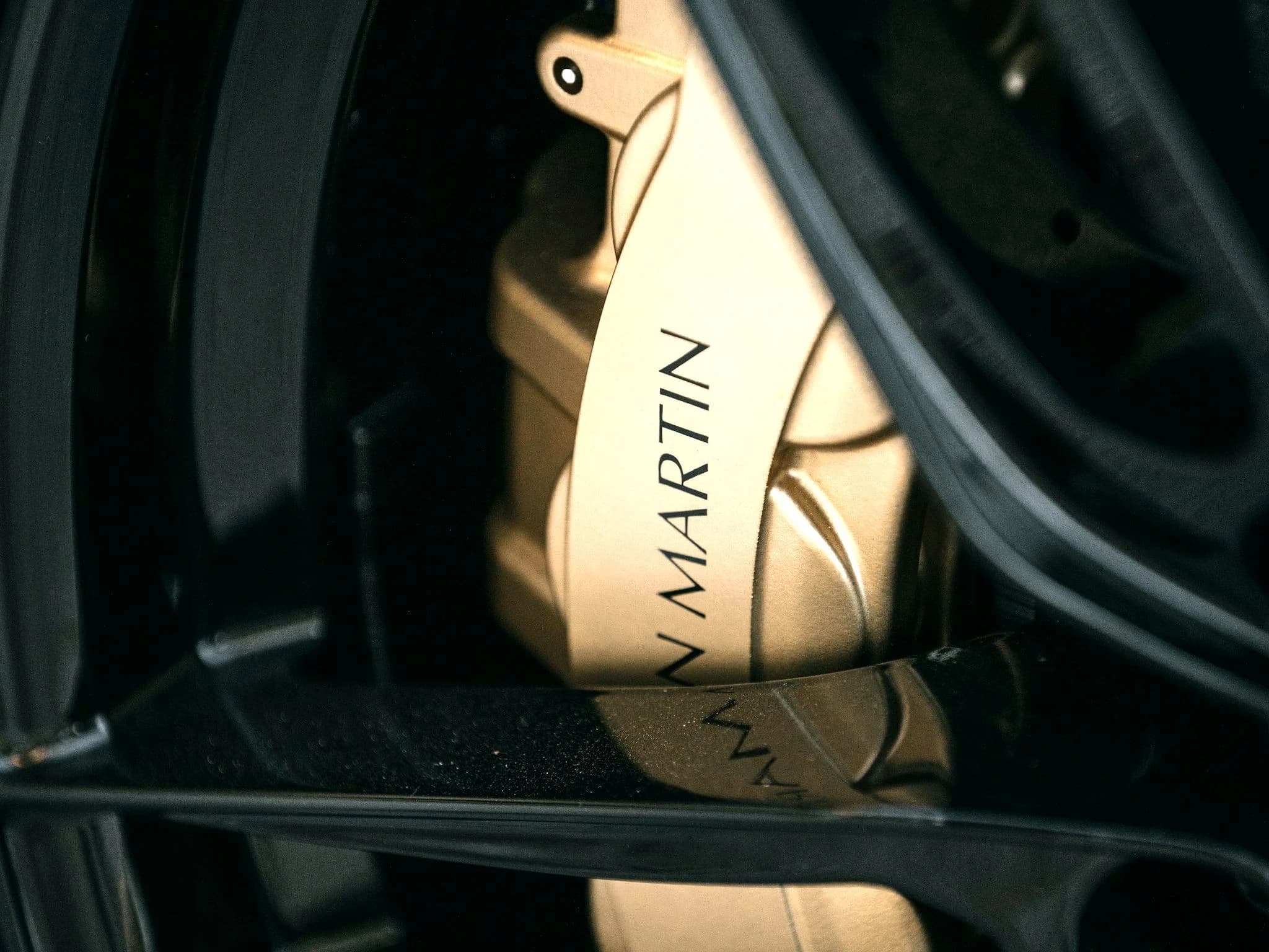A gold Aston Martin brake caliper seen through the spokes of a dark alloy wheel