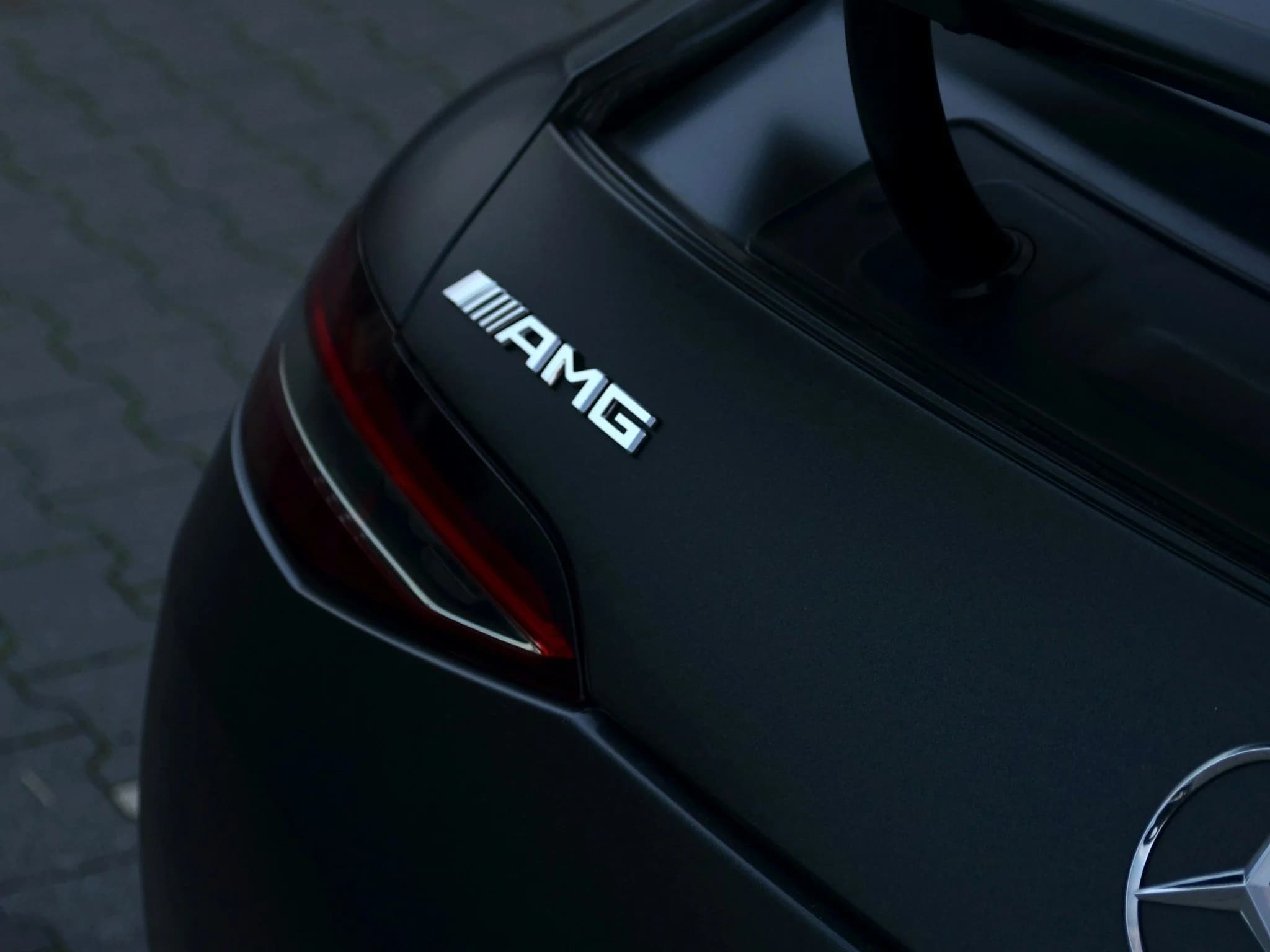 The rear deck of a matte black Mercedes with the AMG badge and part of a tail lamp catching light