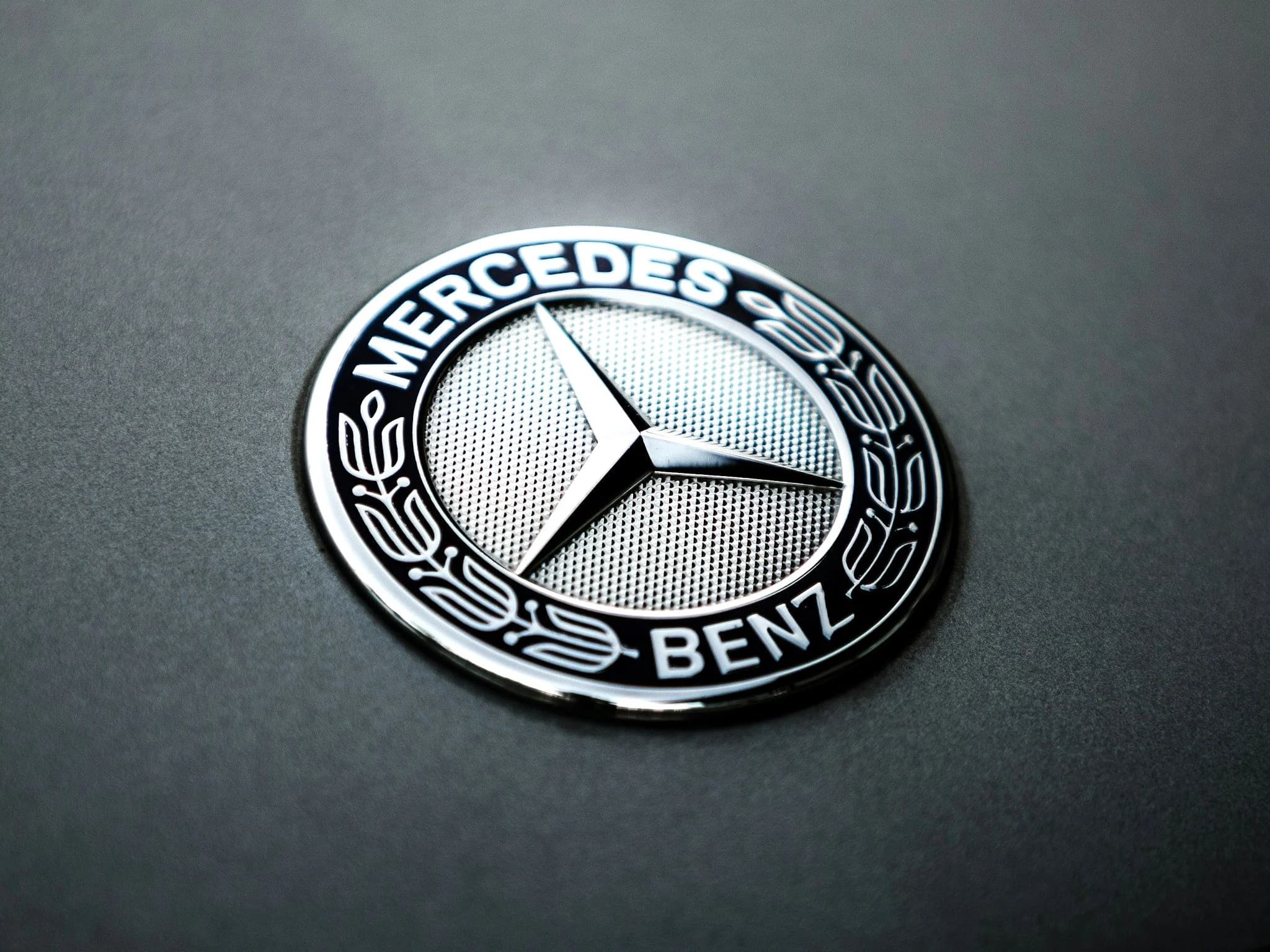 A Mercedes-Benz roundel badge lying against a matte dark panel under a single soft light