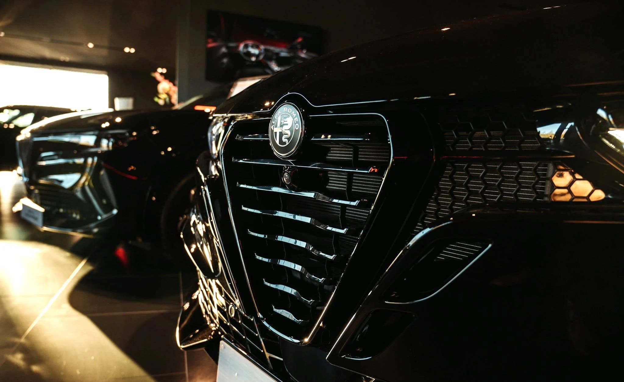 The chrome grille of a dark Alfa Romeo lit from one side inside a showroom