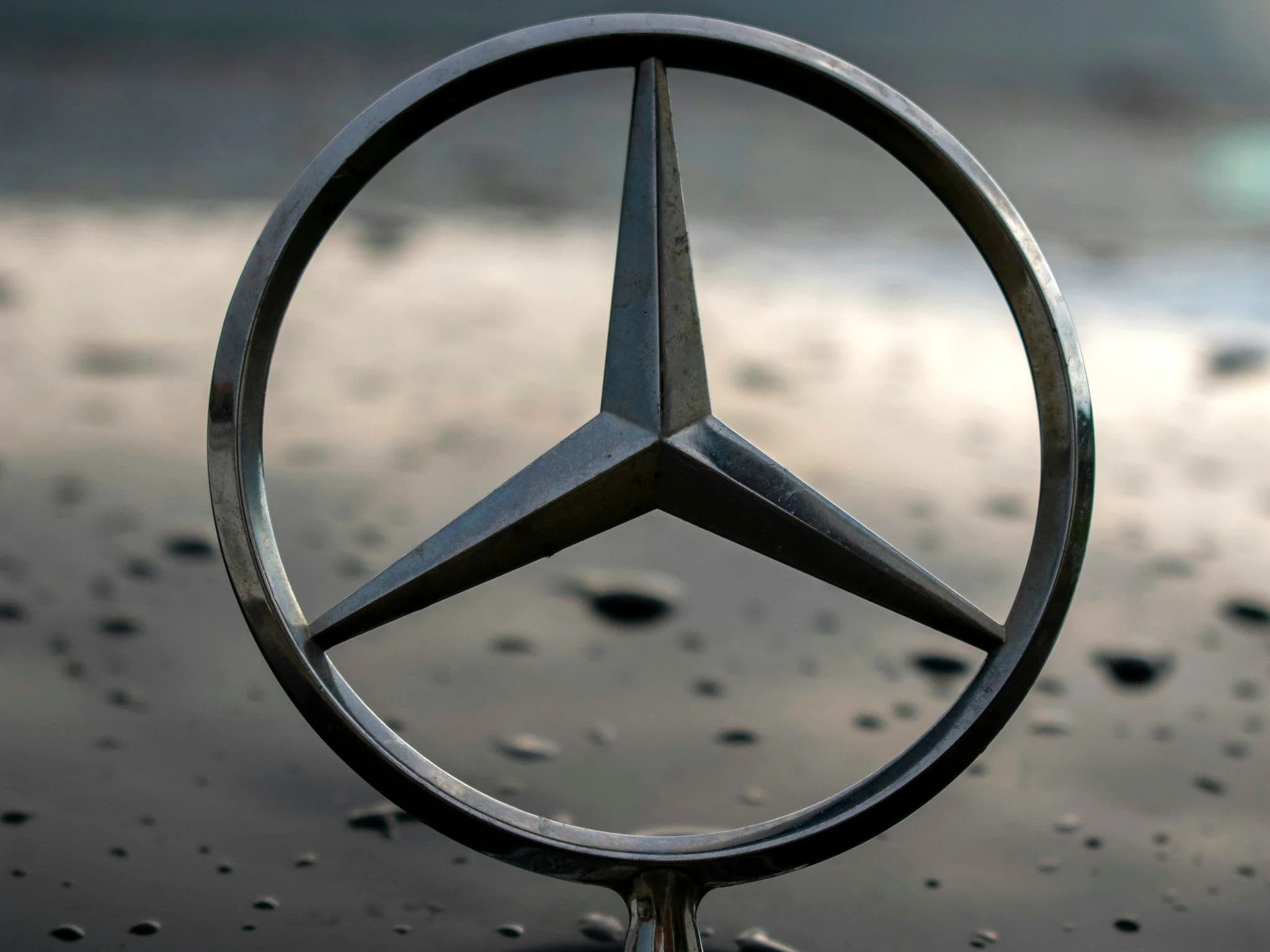 The upright three-pointed Mercedes star on a bonnet with rain beaded on the paint behind it