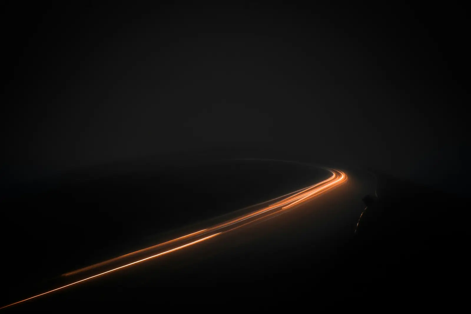 A single ember-coloured light trail curving away through near-total darkness, long exposure