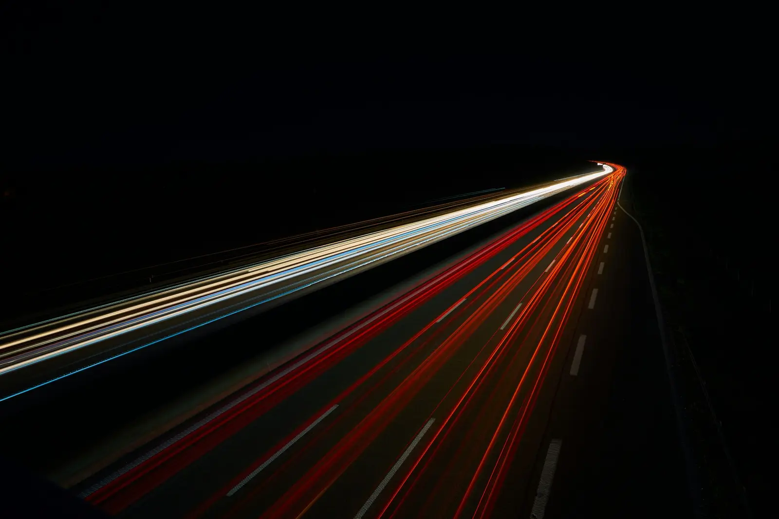 Long-exposure light trails on a night motorway, pale one way and ember the other, against black