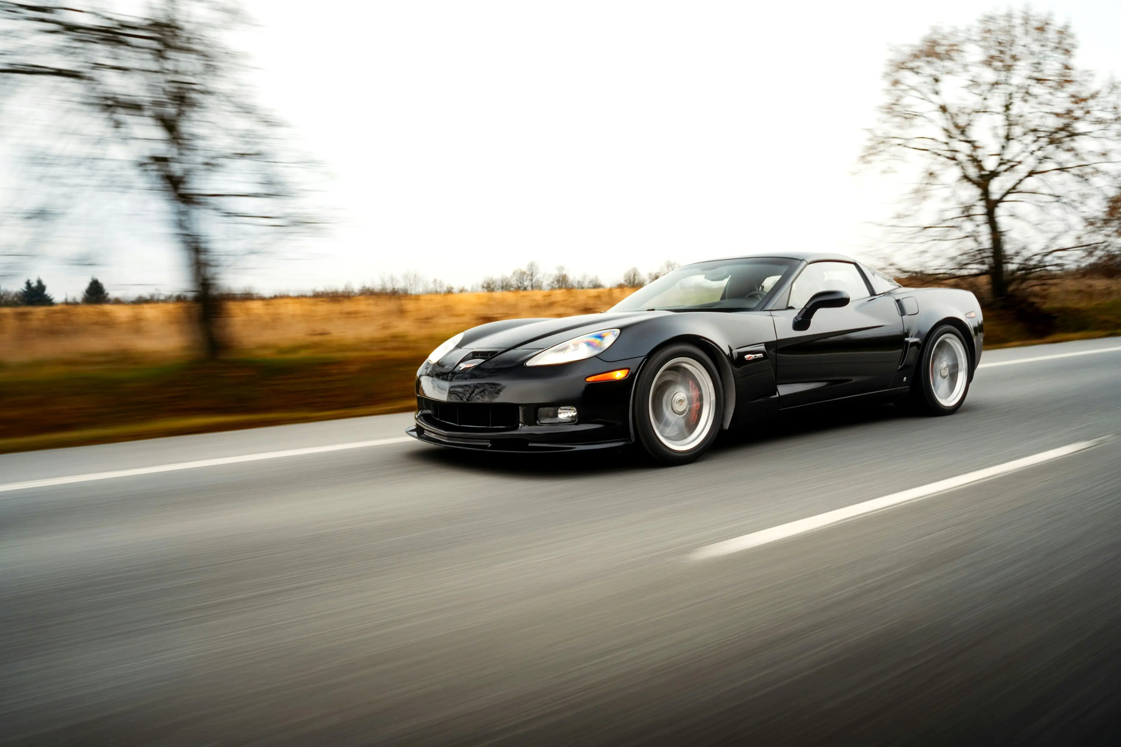 A black Corvette photographed at speed on a country road, the background blurred by the pan
