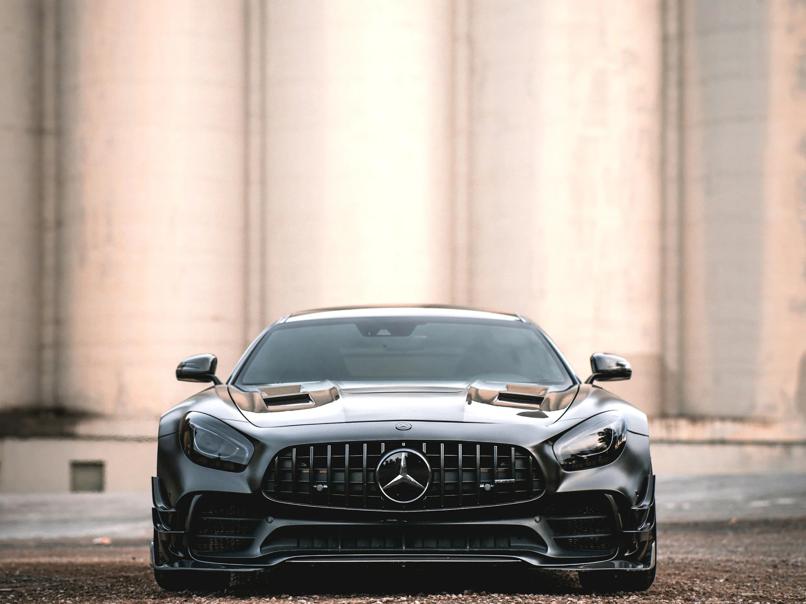 A dark grey Mercedes-AMG GT R seen head on, its Panamericana grille and bonnet vents lit against pale concrete silos