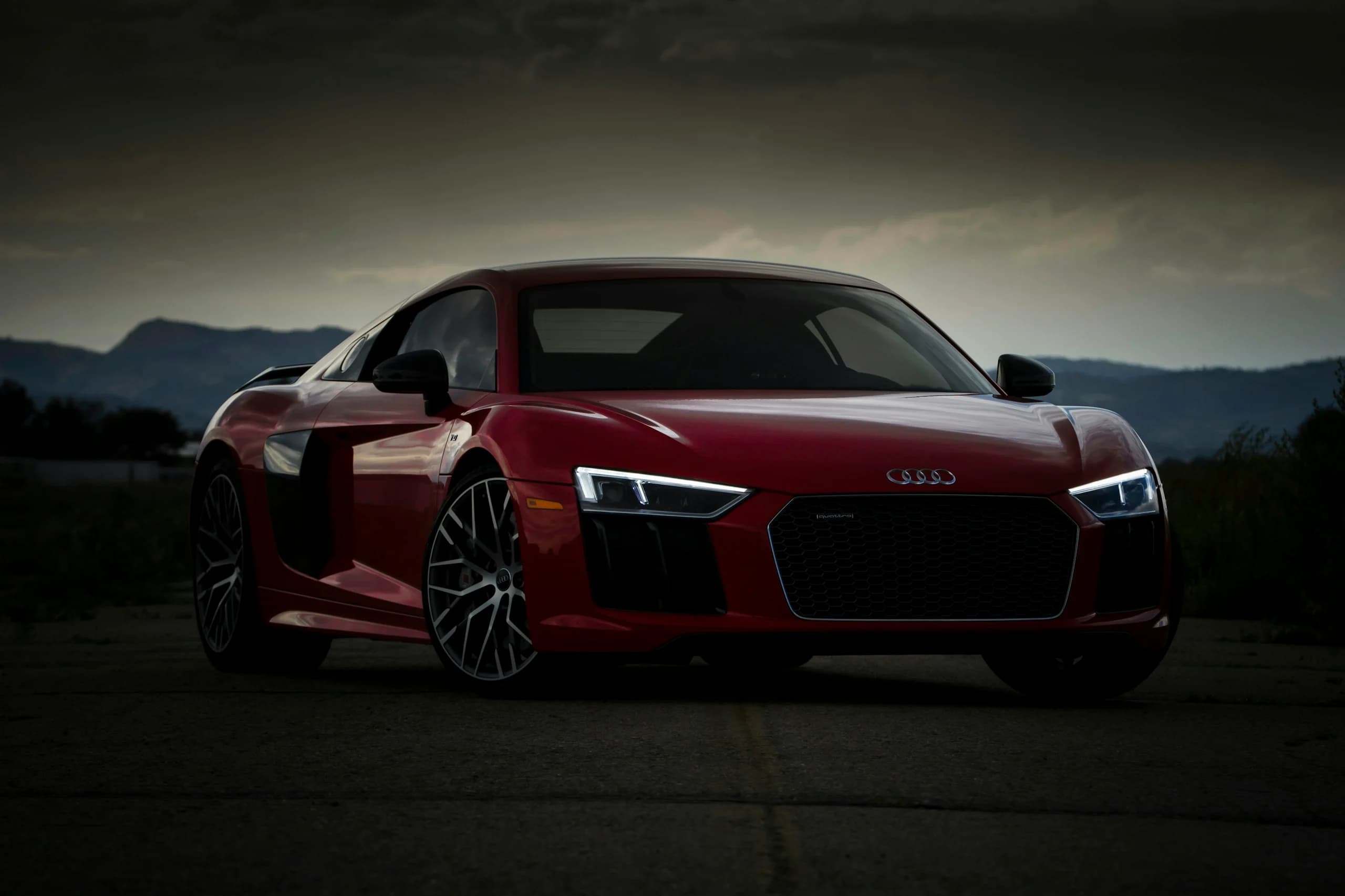 A red Audi R8 photographed head on at dusk on a desert road, the four rings centred on the grille and mountains behind