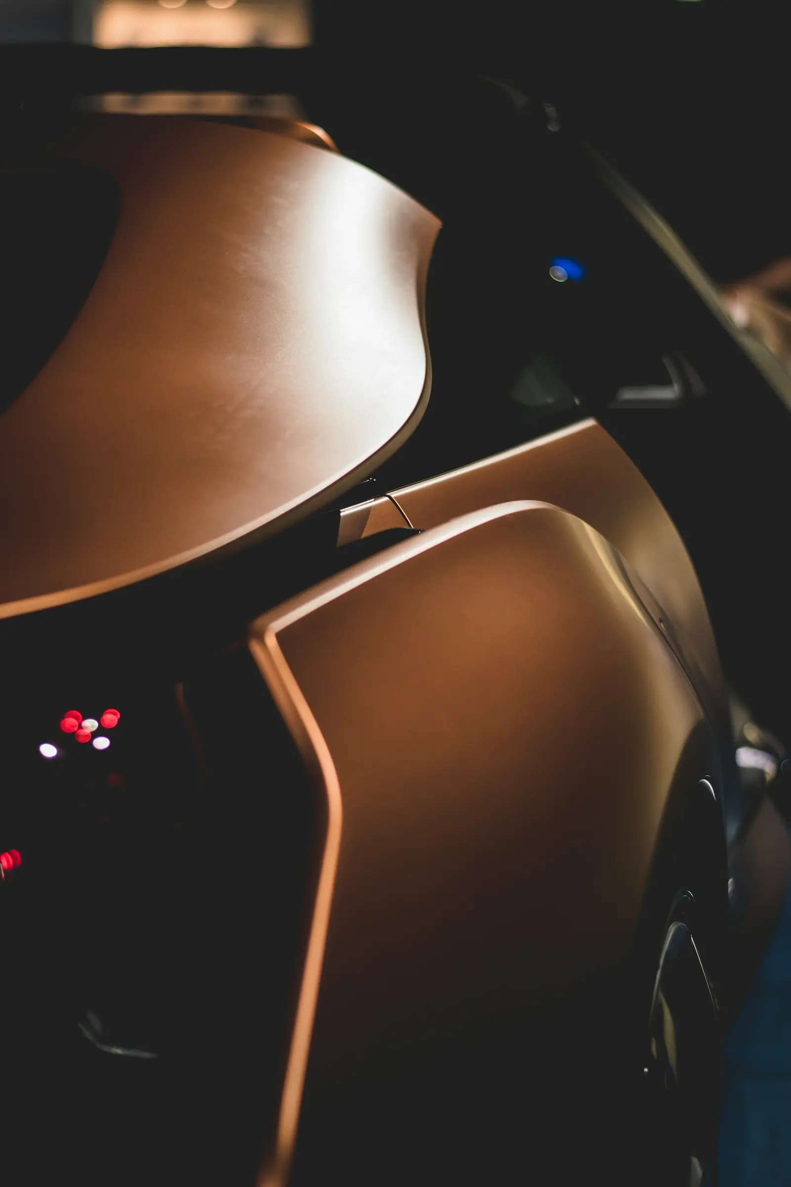 Macro of a sculpted bronze body panel, rim-lit against black, its curve holding a single highlight