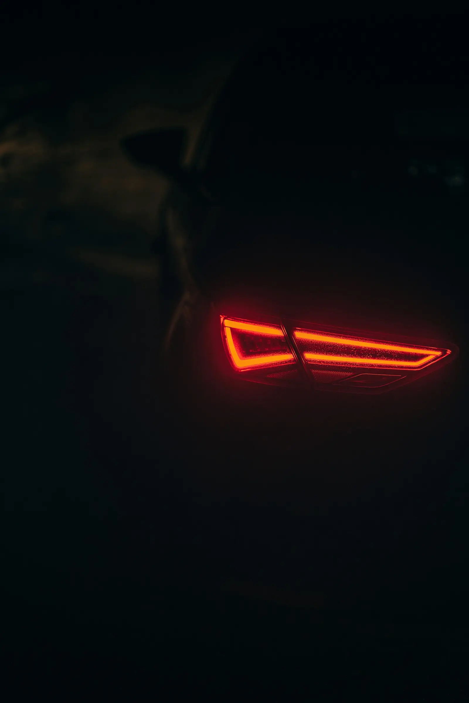 A single red rear lamp signature glowing in darkness, the body around it lost to black