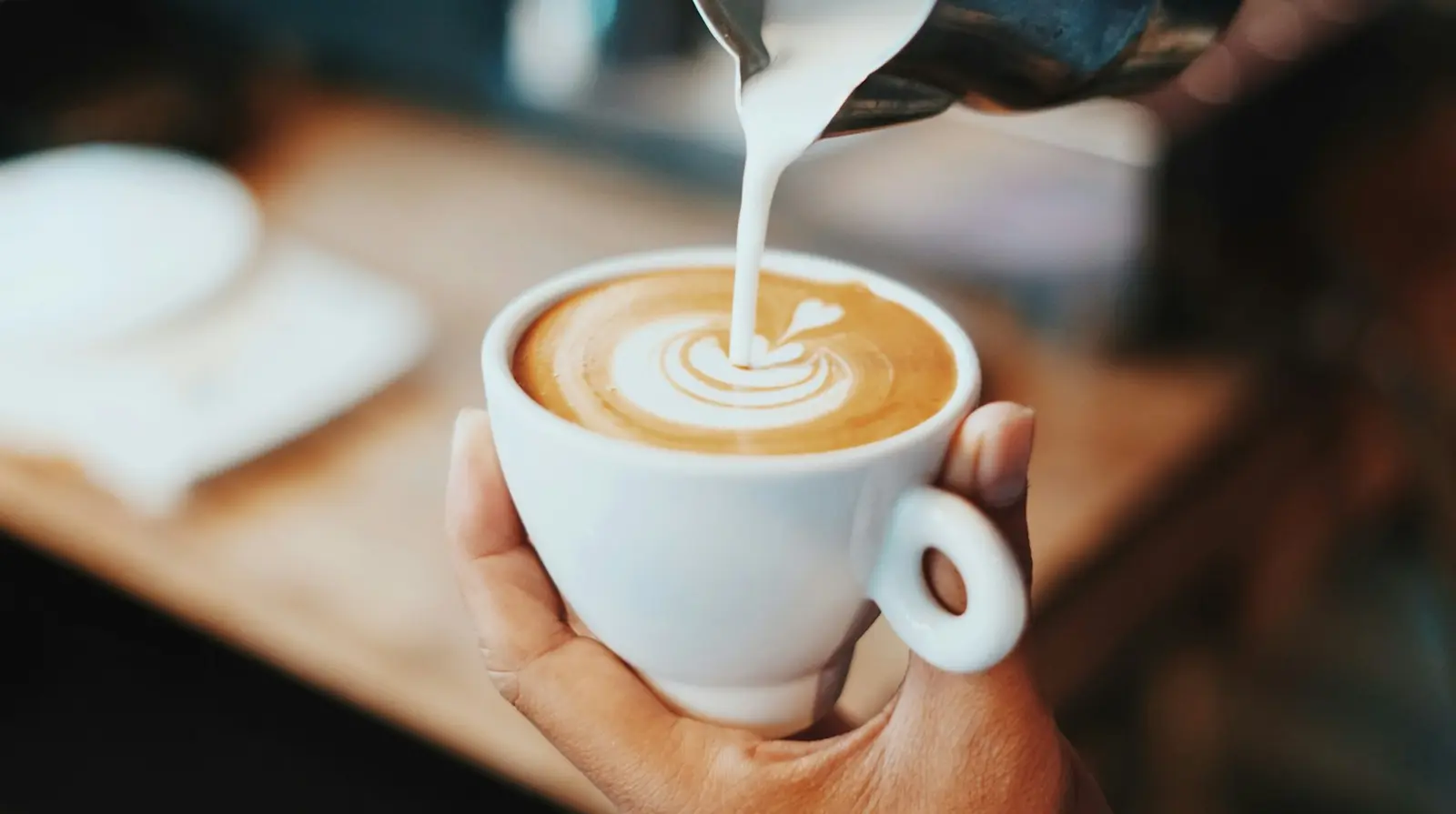 Steamed milk being poured into a flat white held in a hand