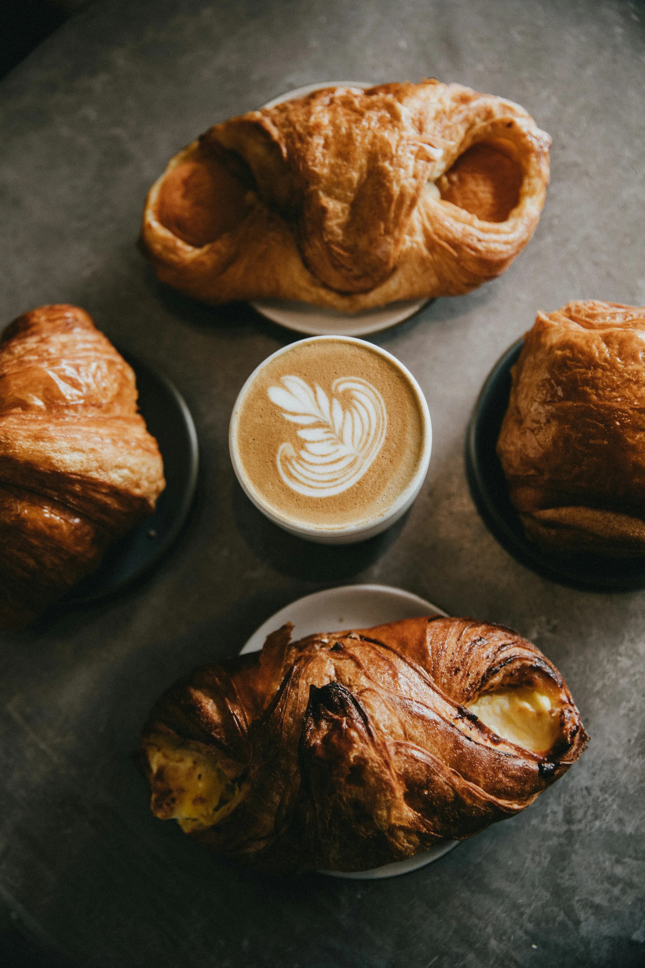 Croissants, a cardamom bun and a cappuccino photographed from above on dark stone
