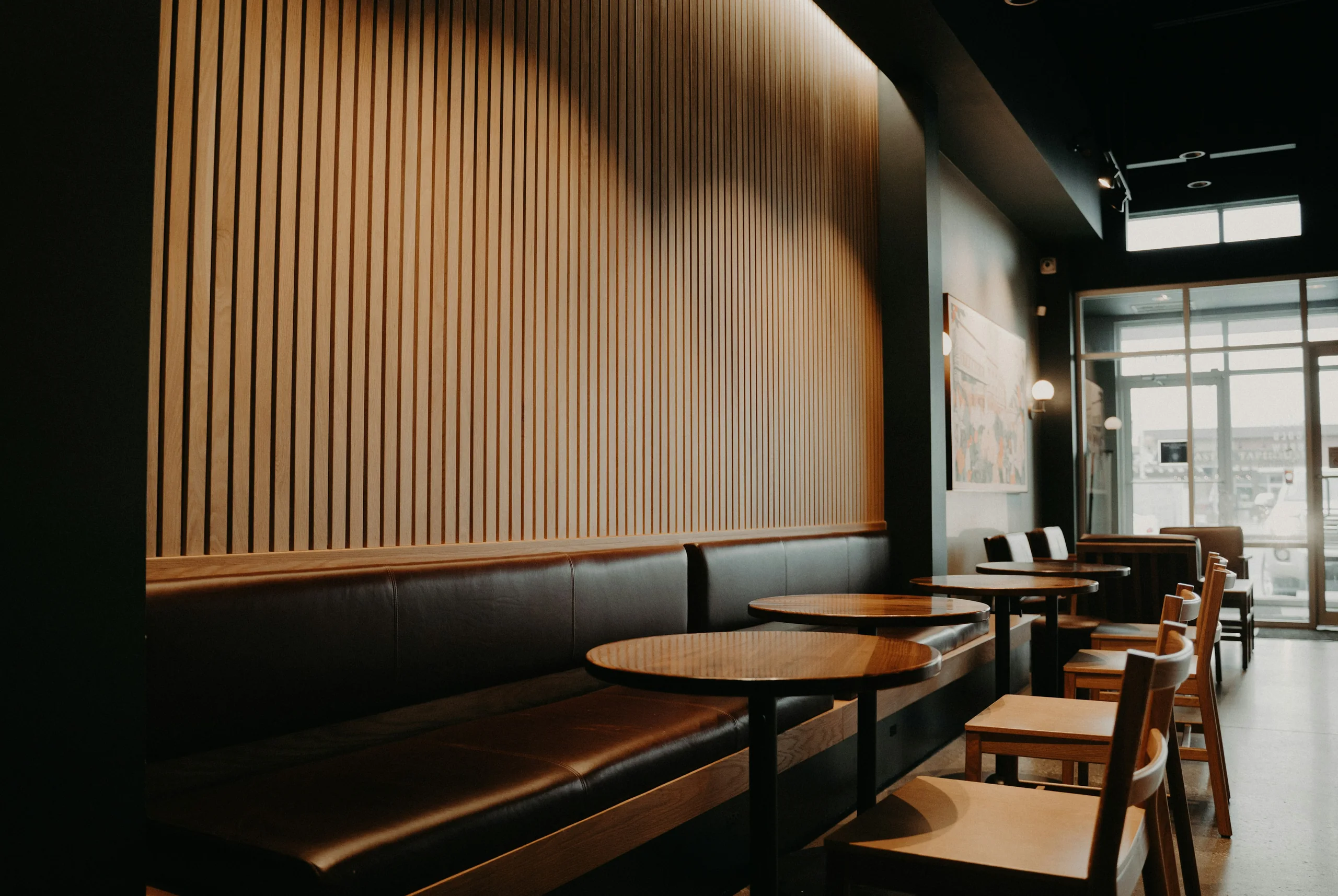 The café room: slatted oak wall, long leather banquette and round timber tables