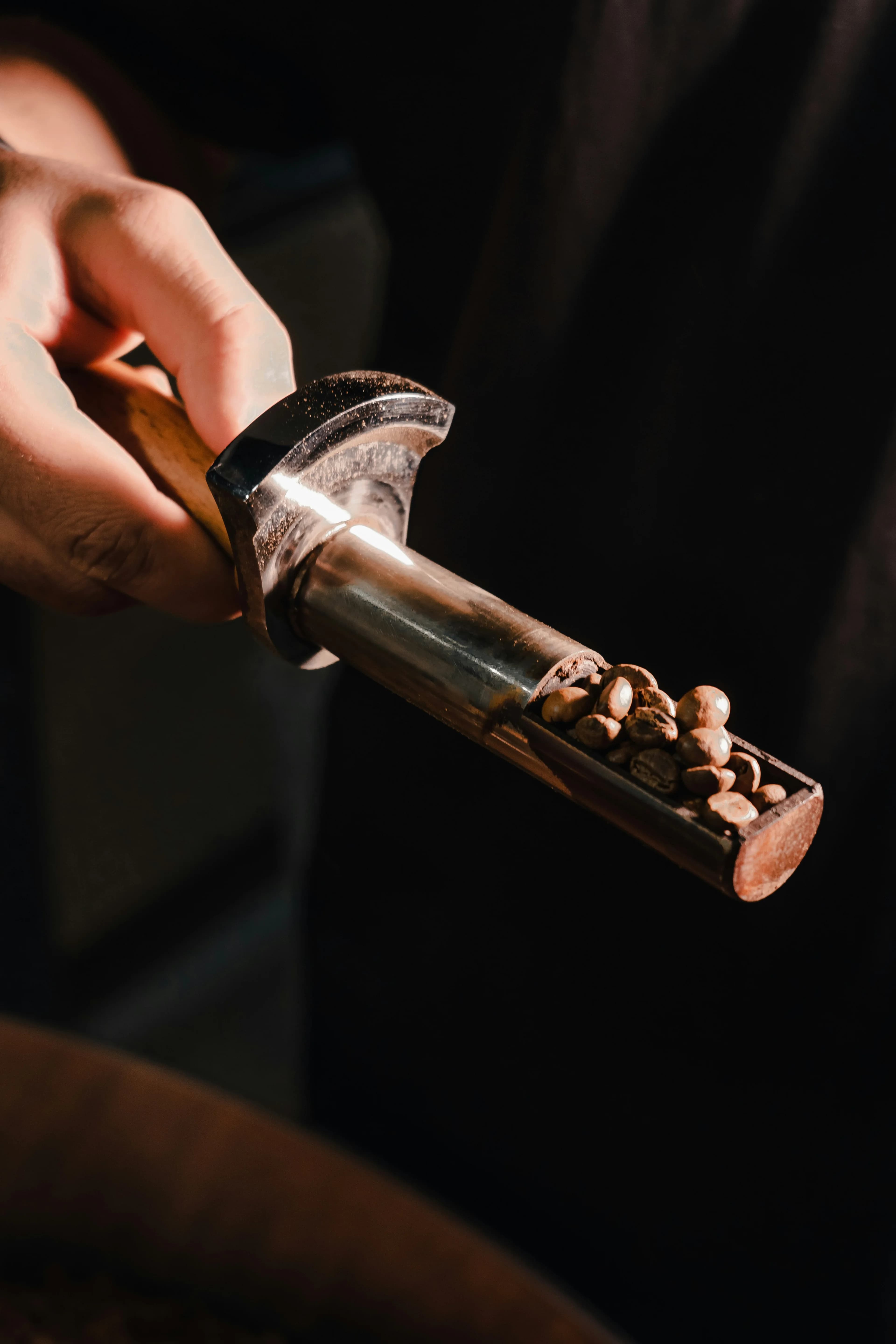 A sample trier of half-roasted beans held out of the drum against the dark of the roastery
