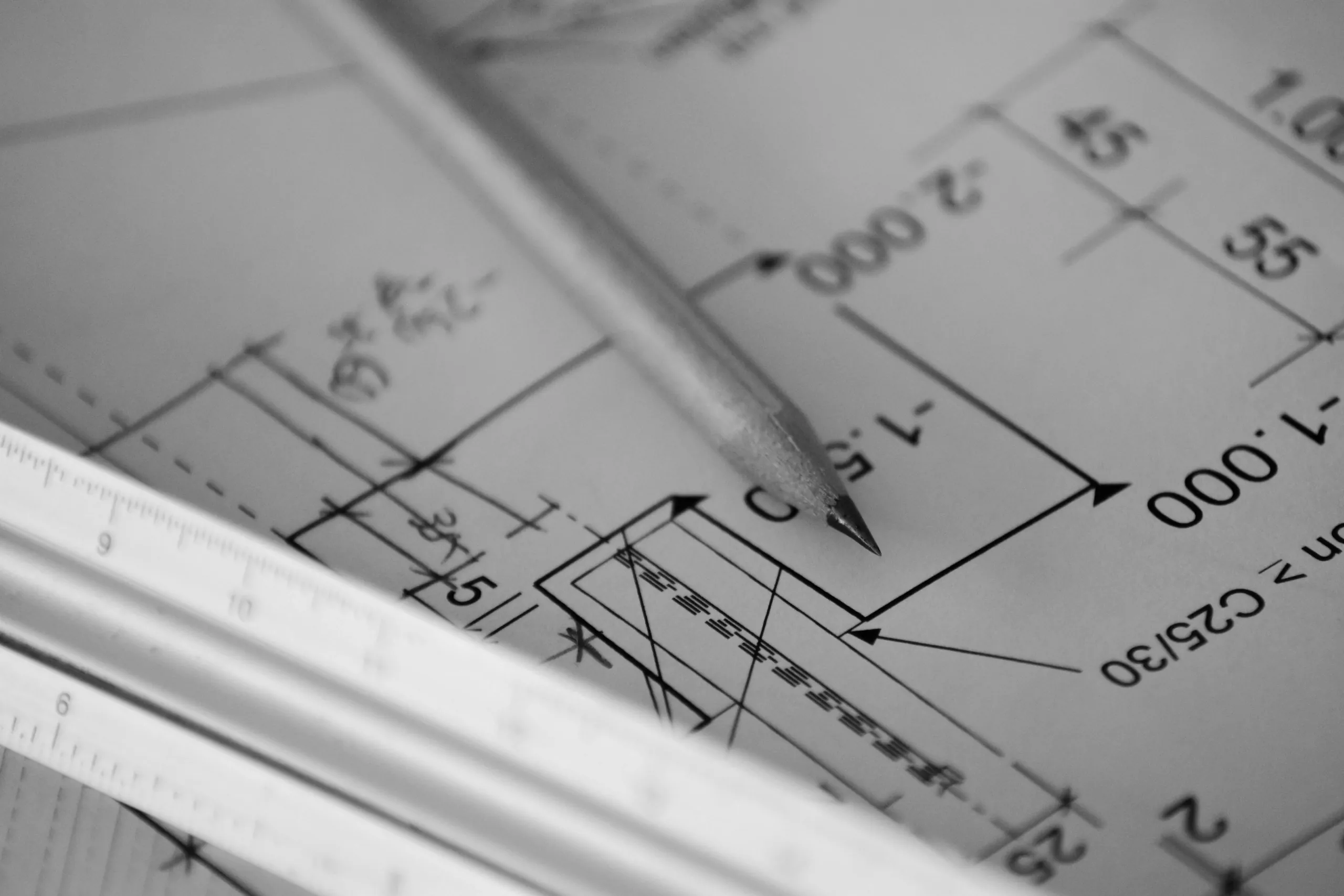 Monochrome close photograph of a dimensioned construction drawing with a pencil and a scale rule lying across it