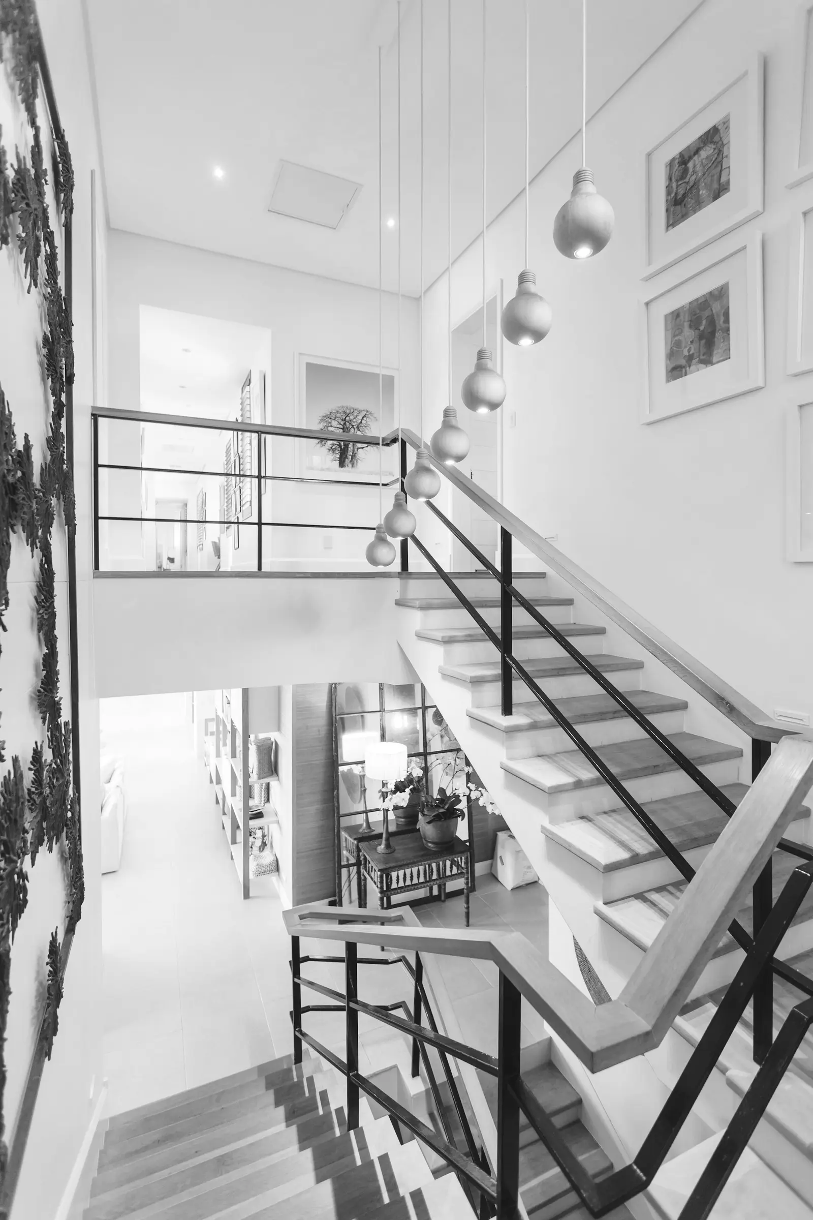 Monochrome photograph of a bright staircase with a thin black steel balustrade and a line of hanging pendant bulbs
