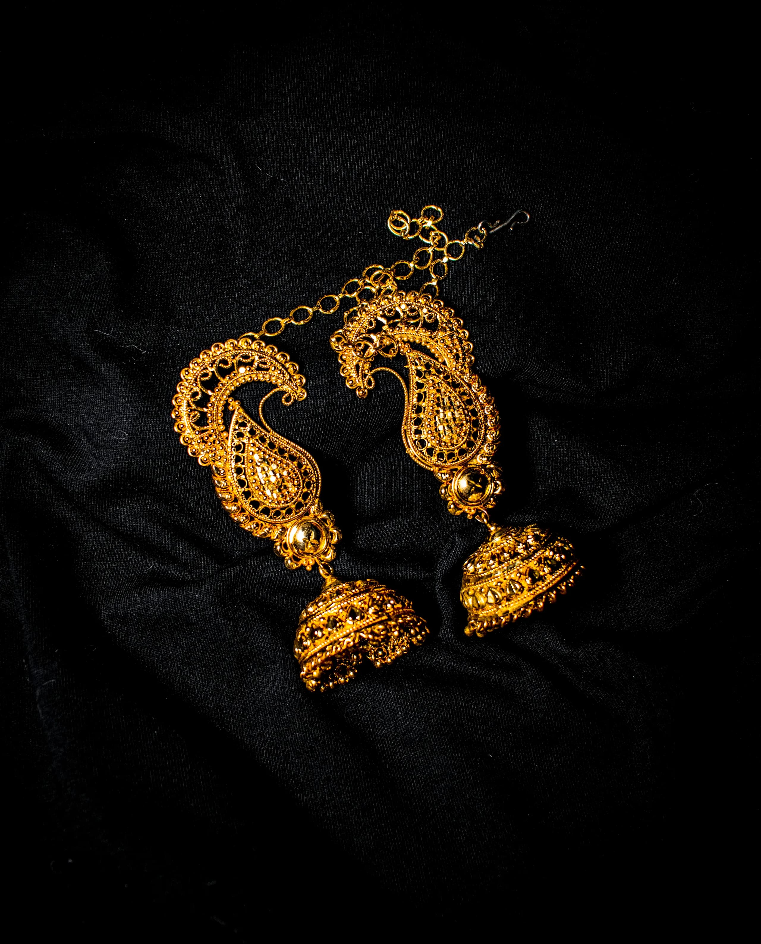 A pair of ornate gold filigree drop earrings laid out on black cloth