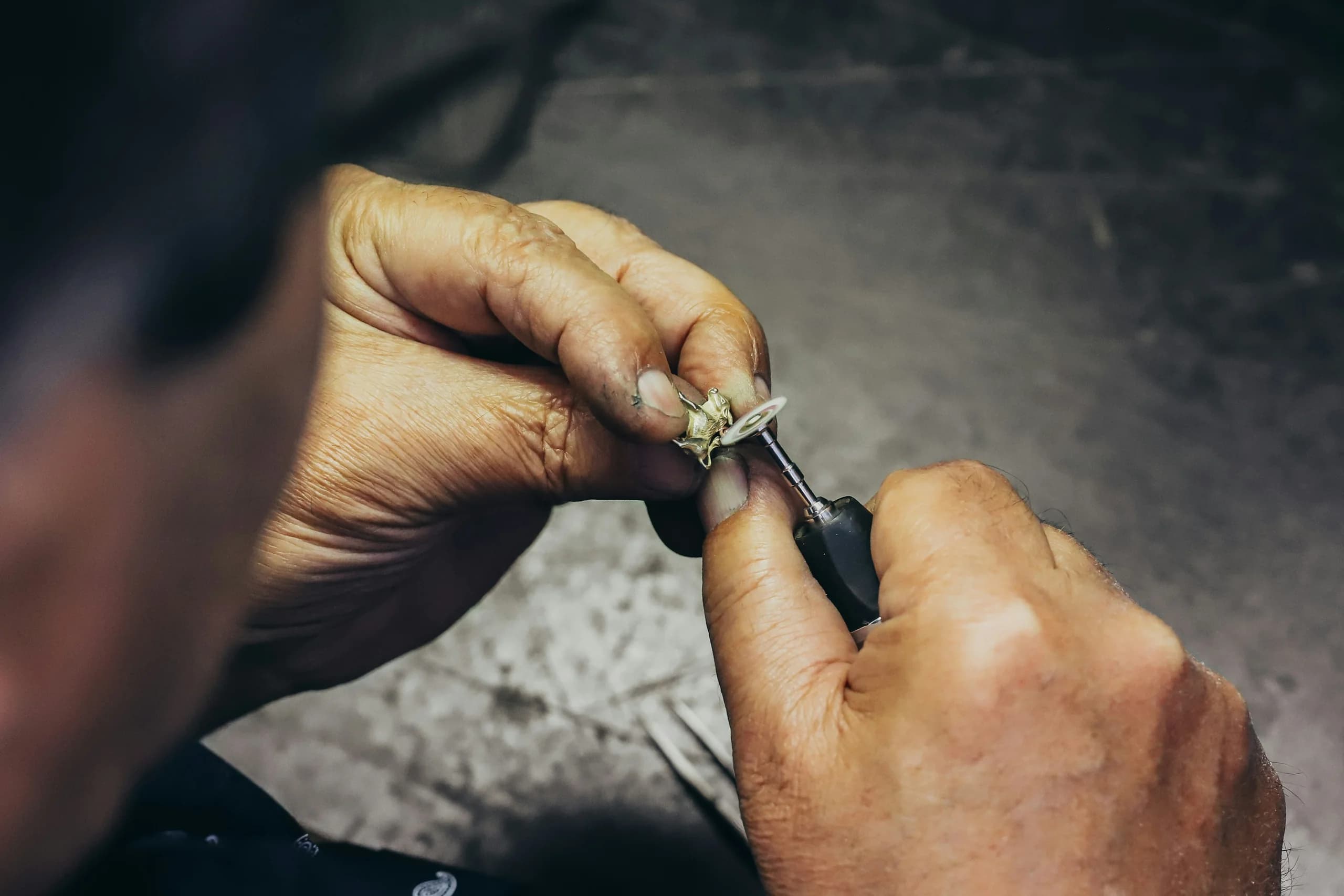 Close-up of two hands taking a small gold piece to a rotary tool fitted with a polishing wheel