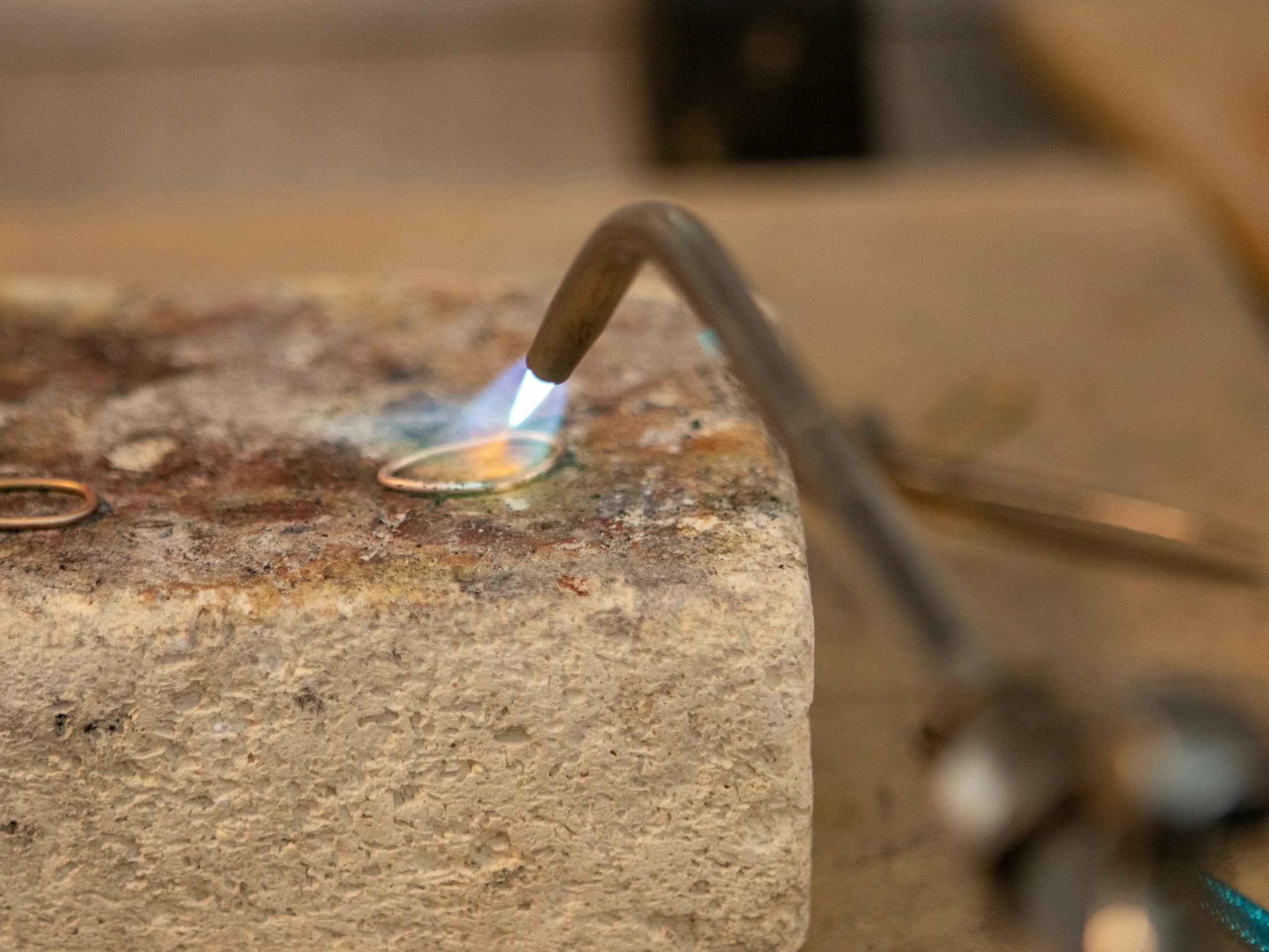 A jeweller's torch playing a small blue flame over a gold band on a soldering block