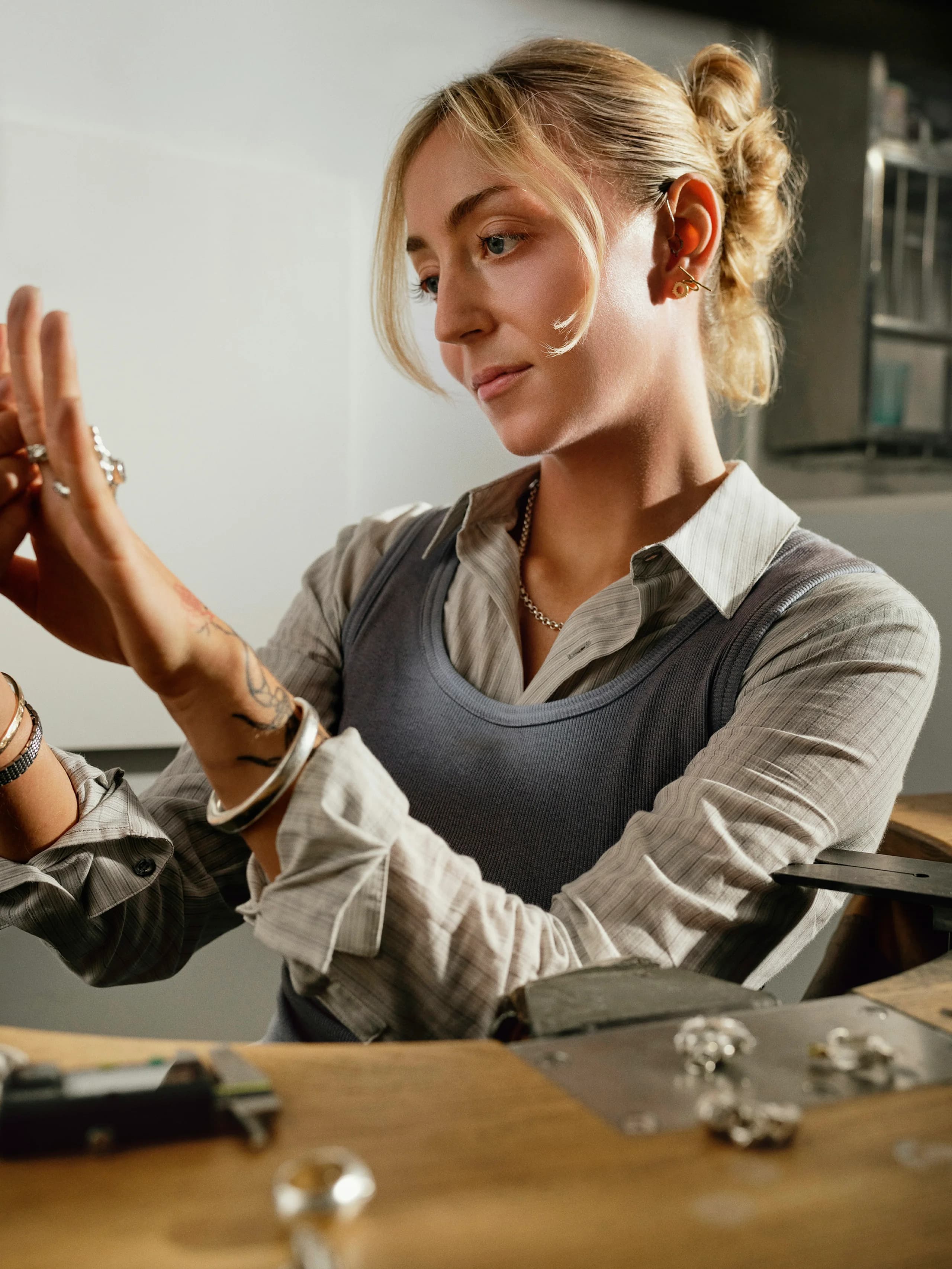 A jeweller at the bench holding a hand up to the light to look at a stack of rings on the fingers