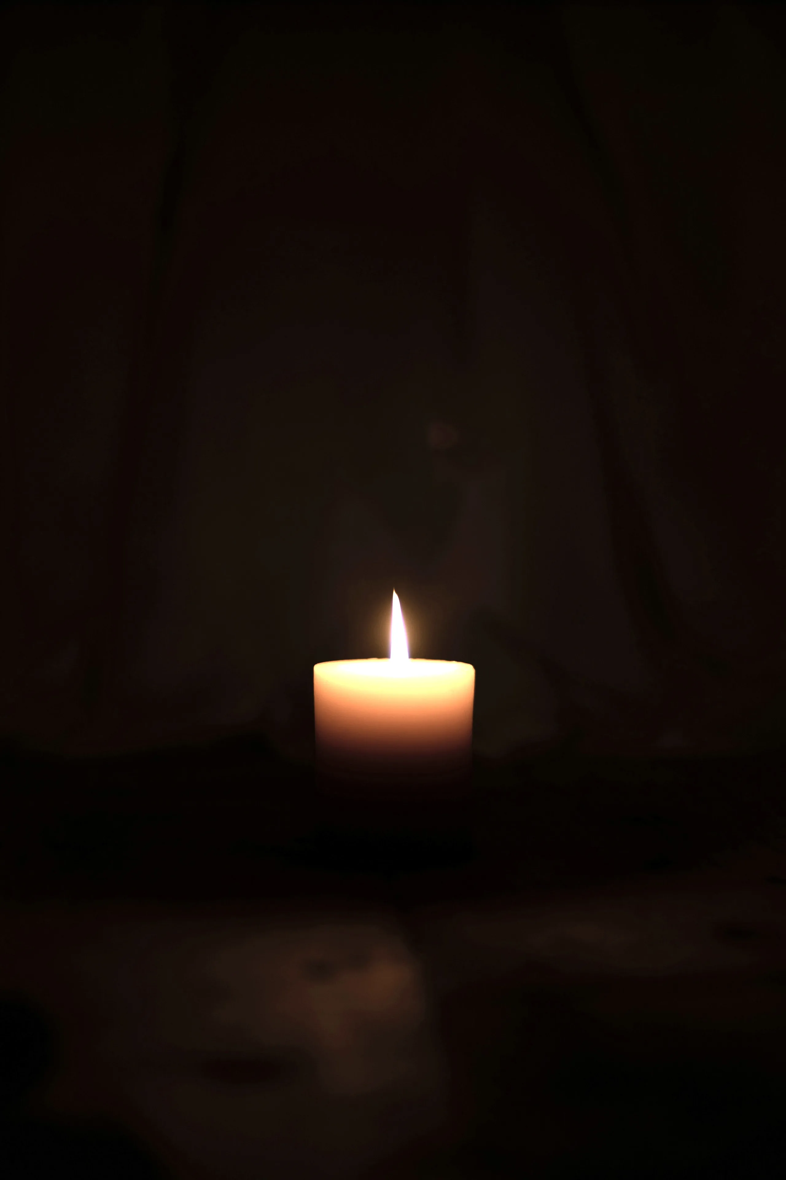 A single lit candle burning in an otherwise completely dark room