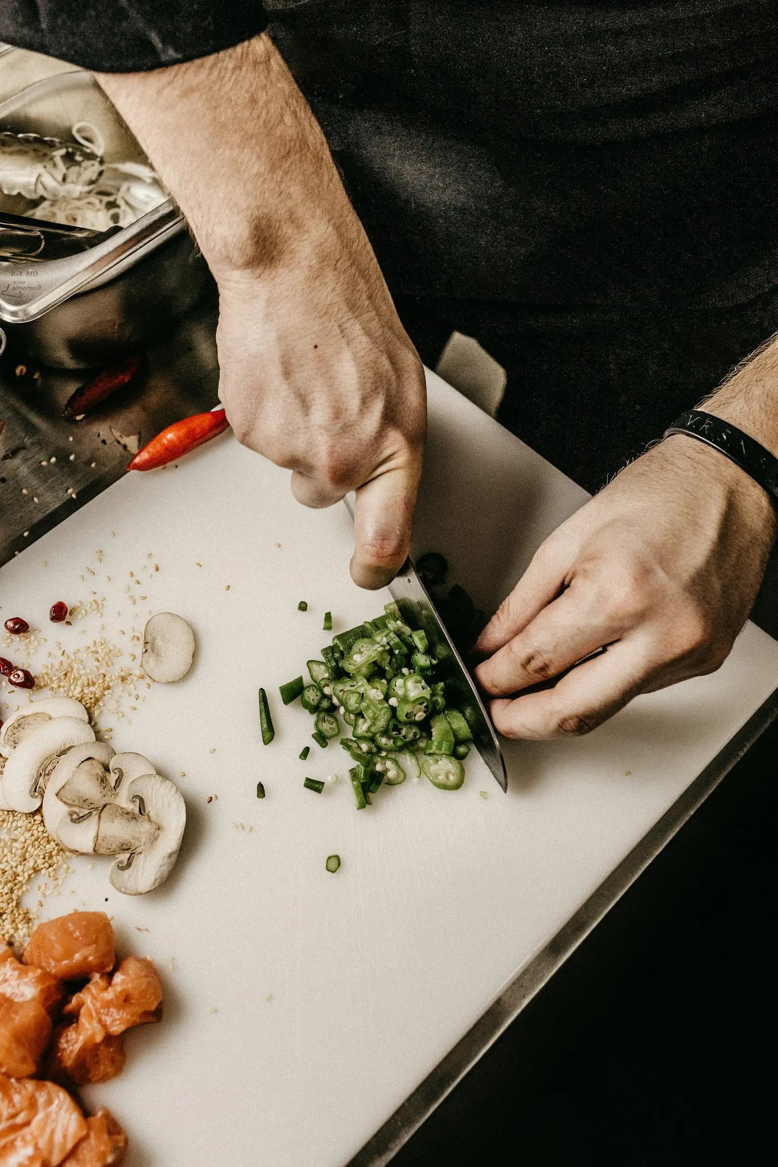 Chef's hands slicing green vegetables on a board at the kitchen pass
