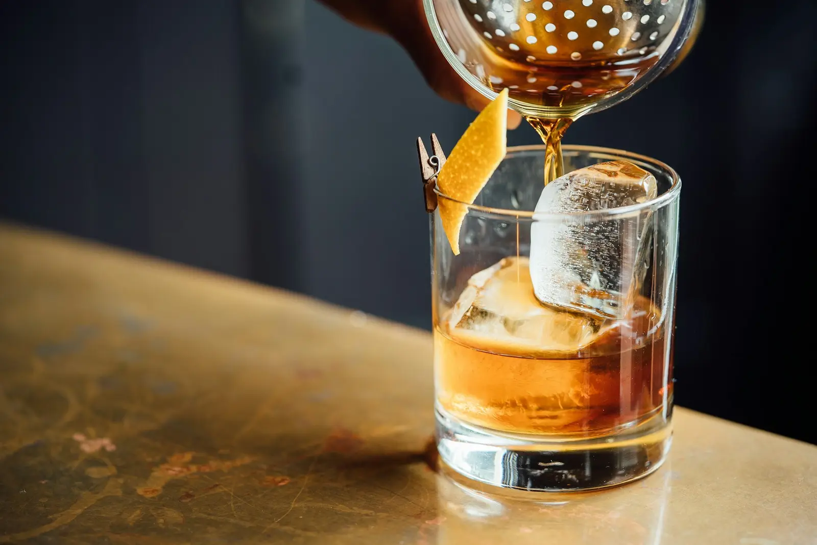 An amber nightcap strained over a large ice cube in a rocks glass