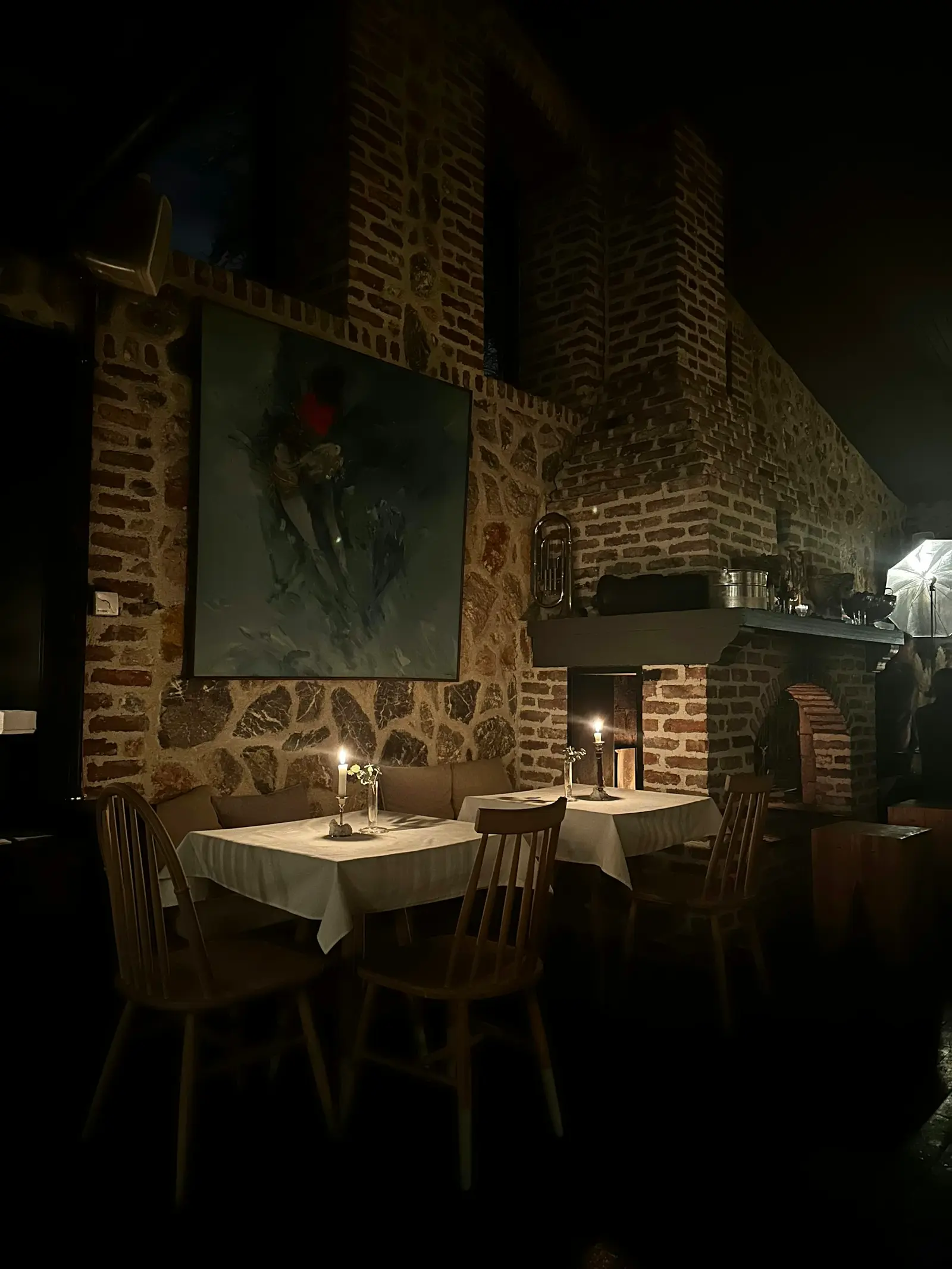 Brick-walled dining room at night, candles burning on white tablecloths