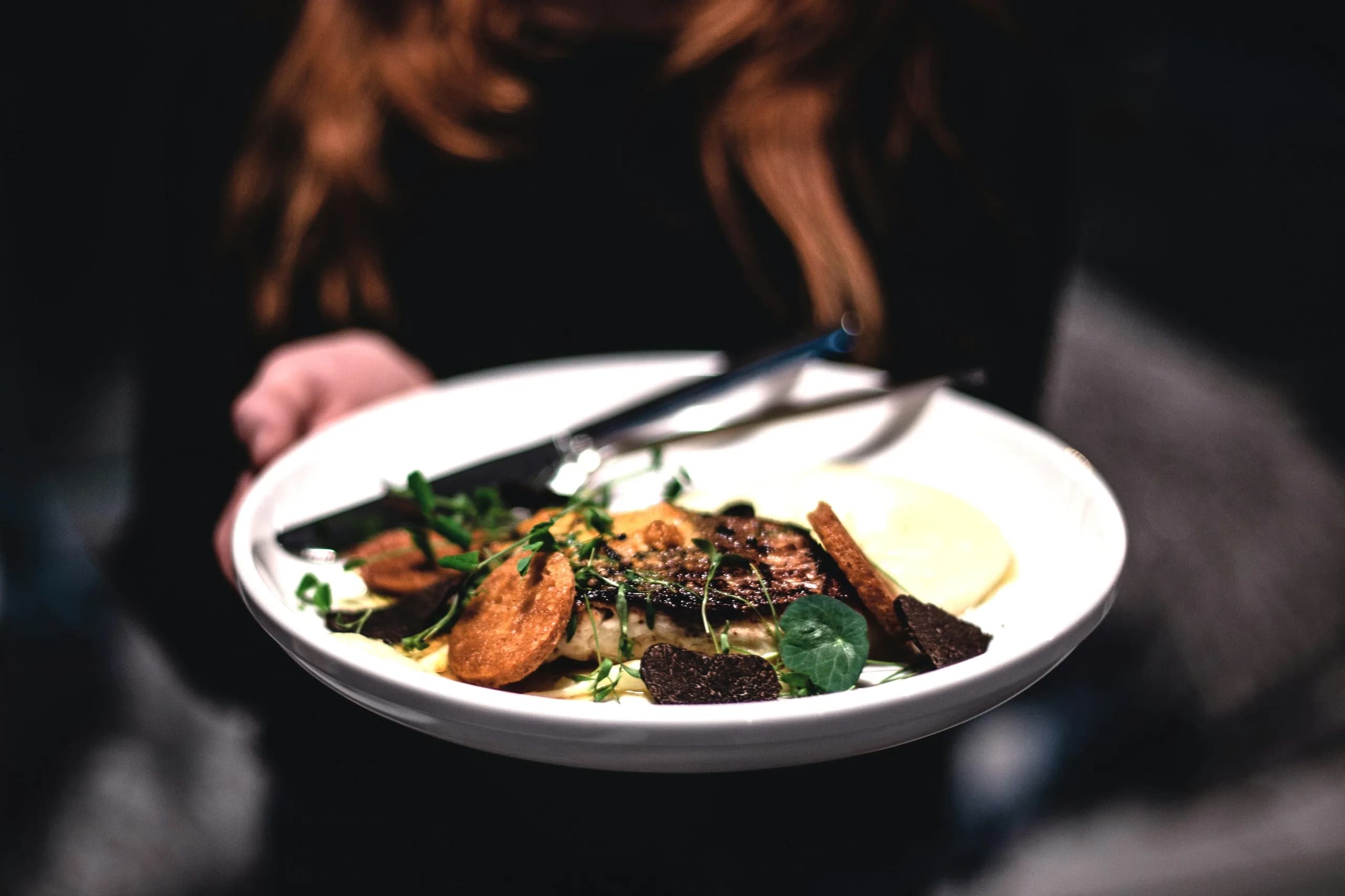 A plated course finished with shaved black truffle, held above a dark table