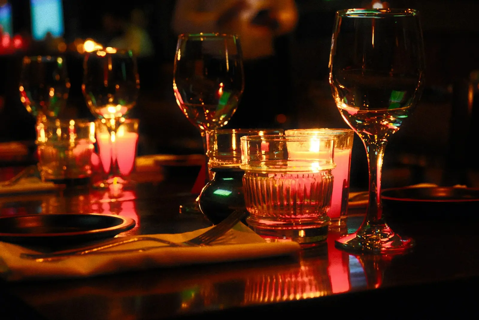Wine glasses and votive candles glowing on a dark set table