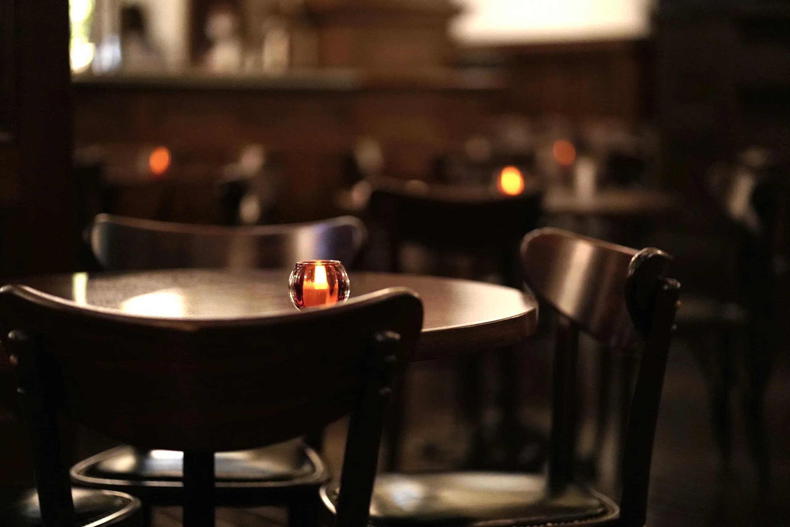 One lit votive on a bare table in a dark dining room, chairs pushed in