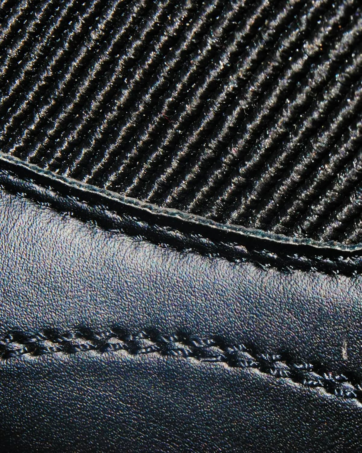 Macro detail of black leather stitching meeting a ribbed textile panel