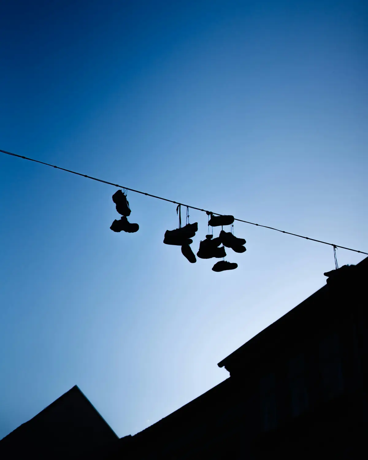 Laced shoes hanging from a power line, silhouetted against a dusk sky