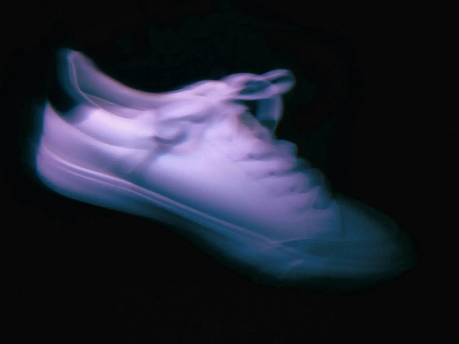 Unbranded low-top sneaker glowing under violet light on a black background