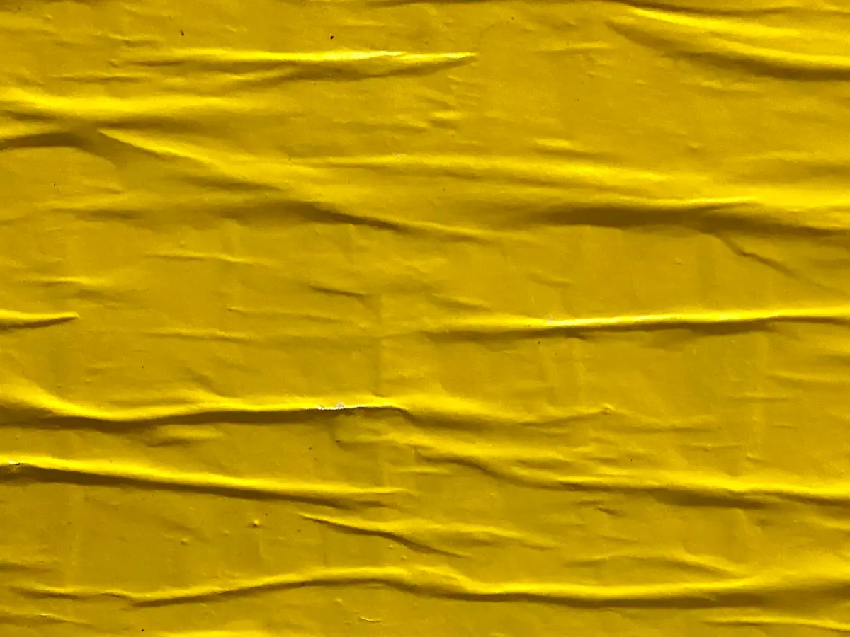 Crumpled bright yellow poster paper pasted flat, creases raking across it.
