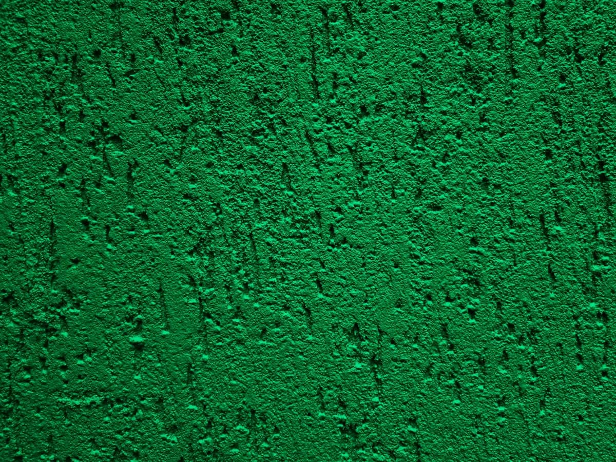 A rough plastered wall painted a saturated acid green, pitted all over.
