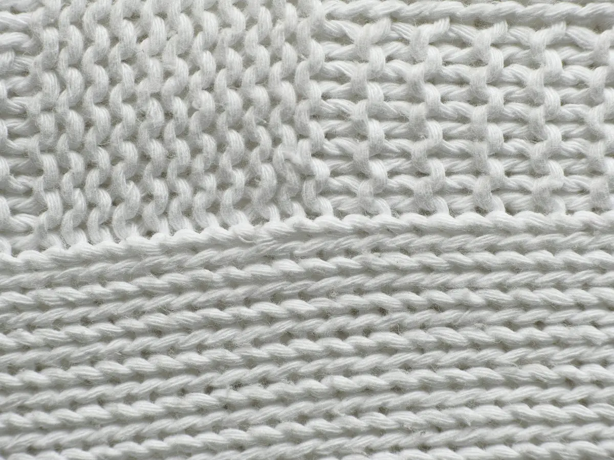 White knitted fabric photographed close, two different stitch gauges meeting in one panel.