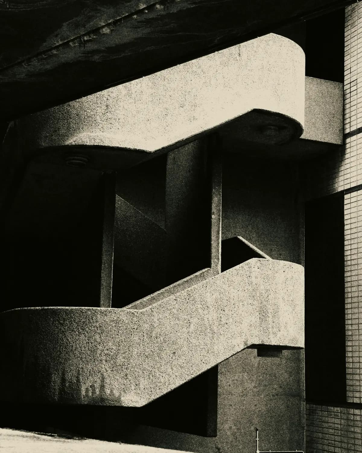 Brutalist concrete stairs and beams in hard sunlight, black and white.