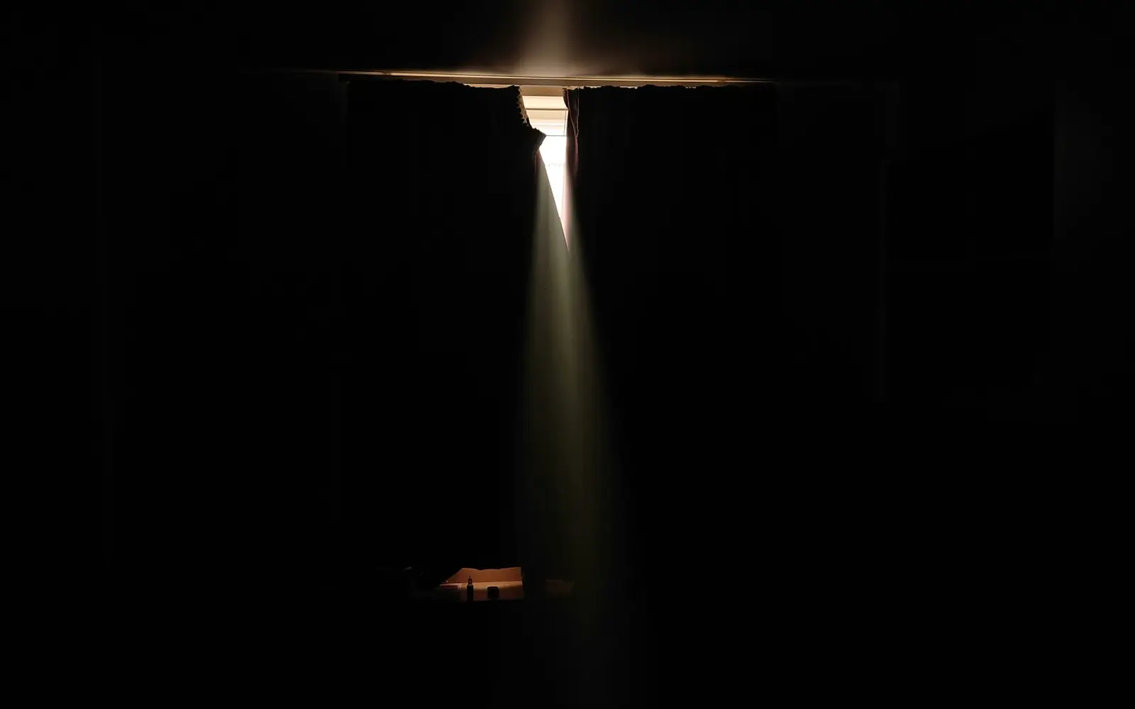 A dark room with a single blade of light falling from a gap in the ceiling.