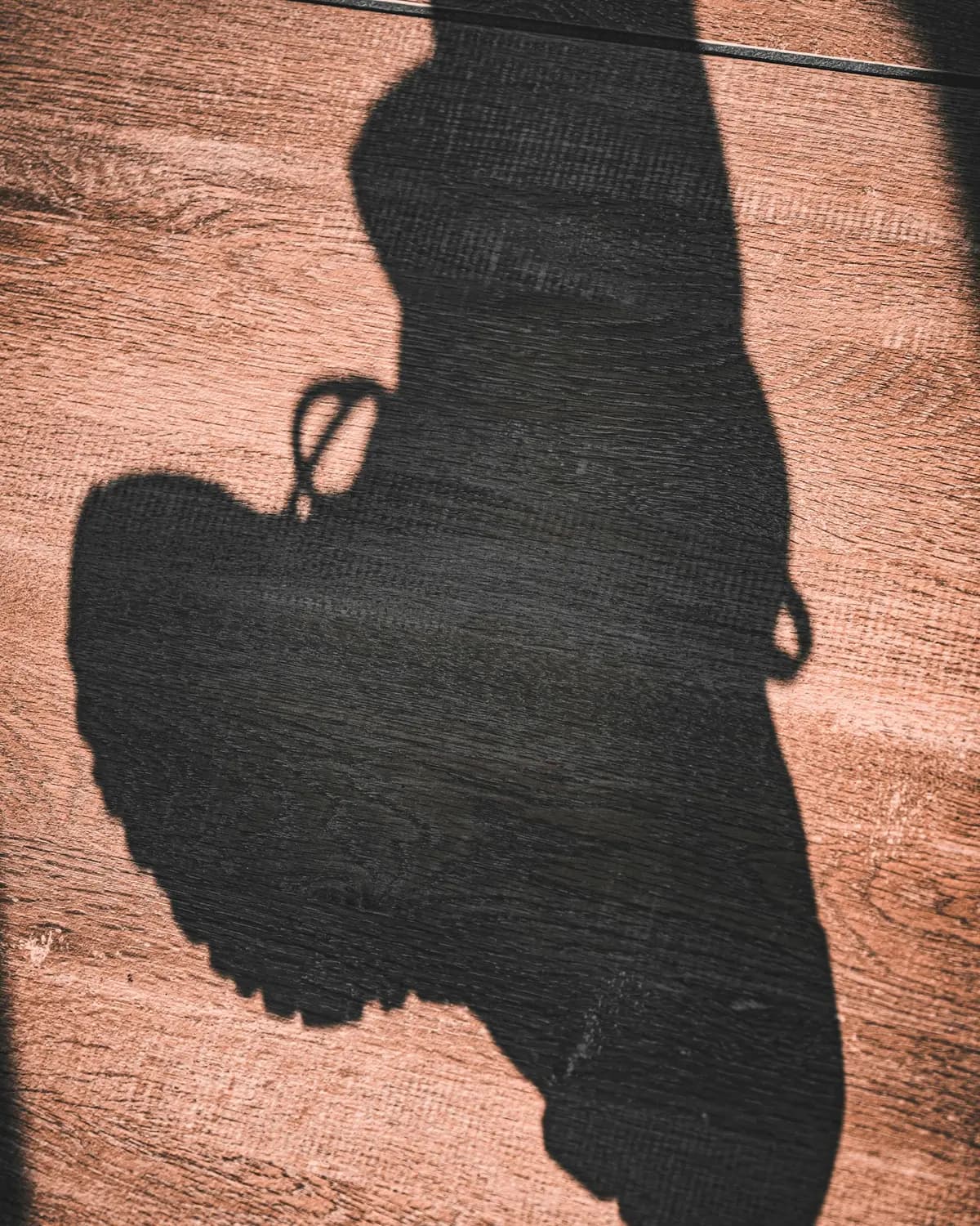 Long shadow of a laced shoe cast across warm timber