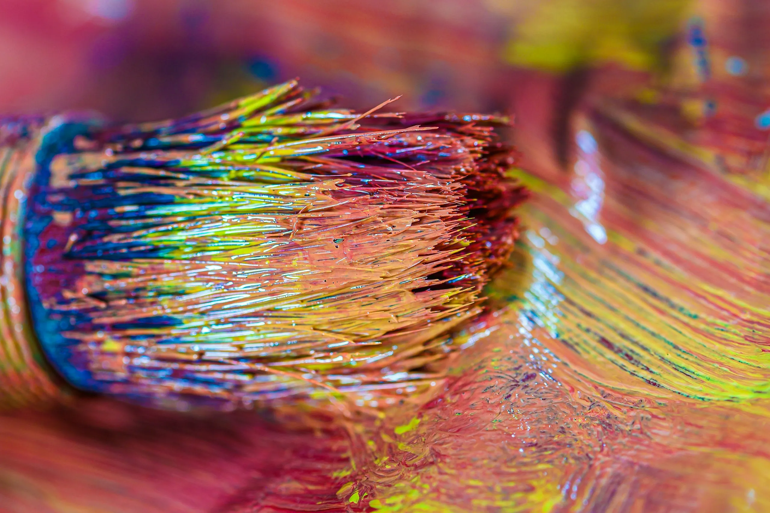 Macro of a brush head loaded with many colours at once, bristles glossy with wet paint