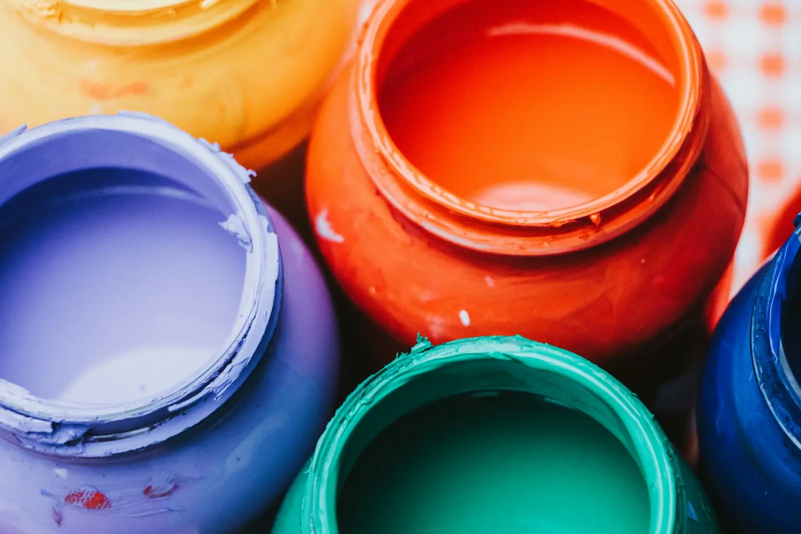 Open jars of paint seen close up — orange, yellow, violet and green, freshly stirred