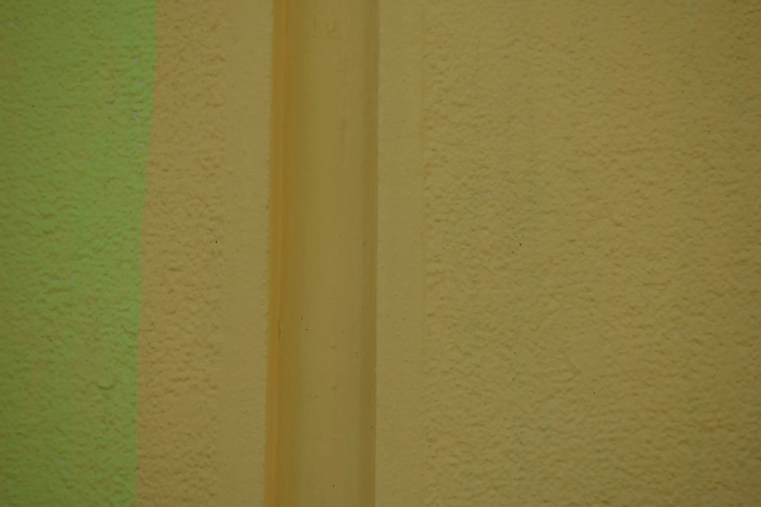 A textured wall carrying two test bands of paint side by side, a pale green against a warm stone colour
