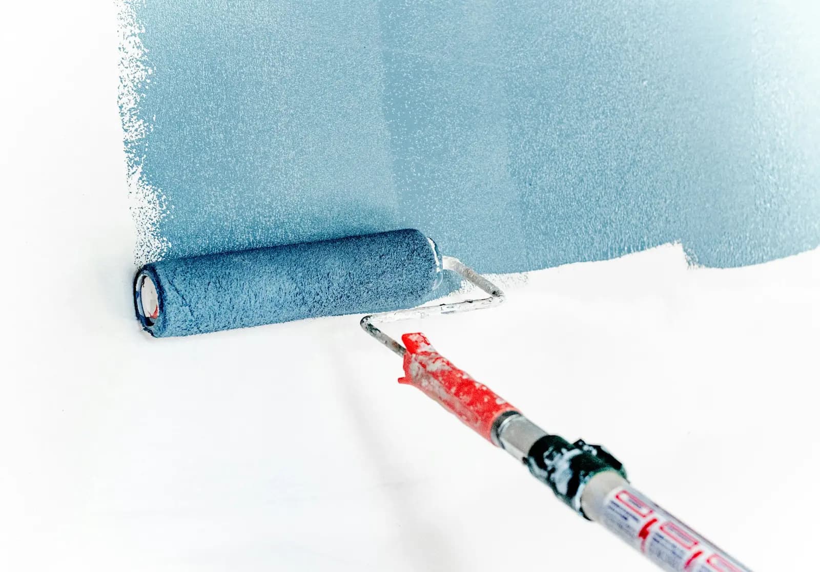Paint roller laying an even coat of dusty blue paint onto a white wall